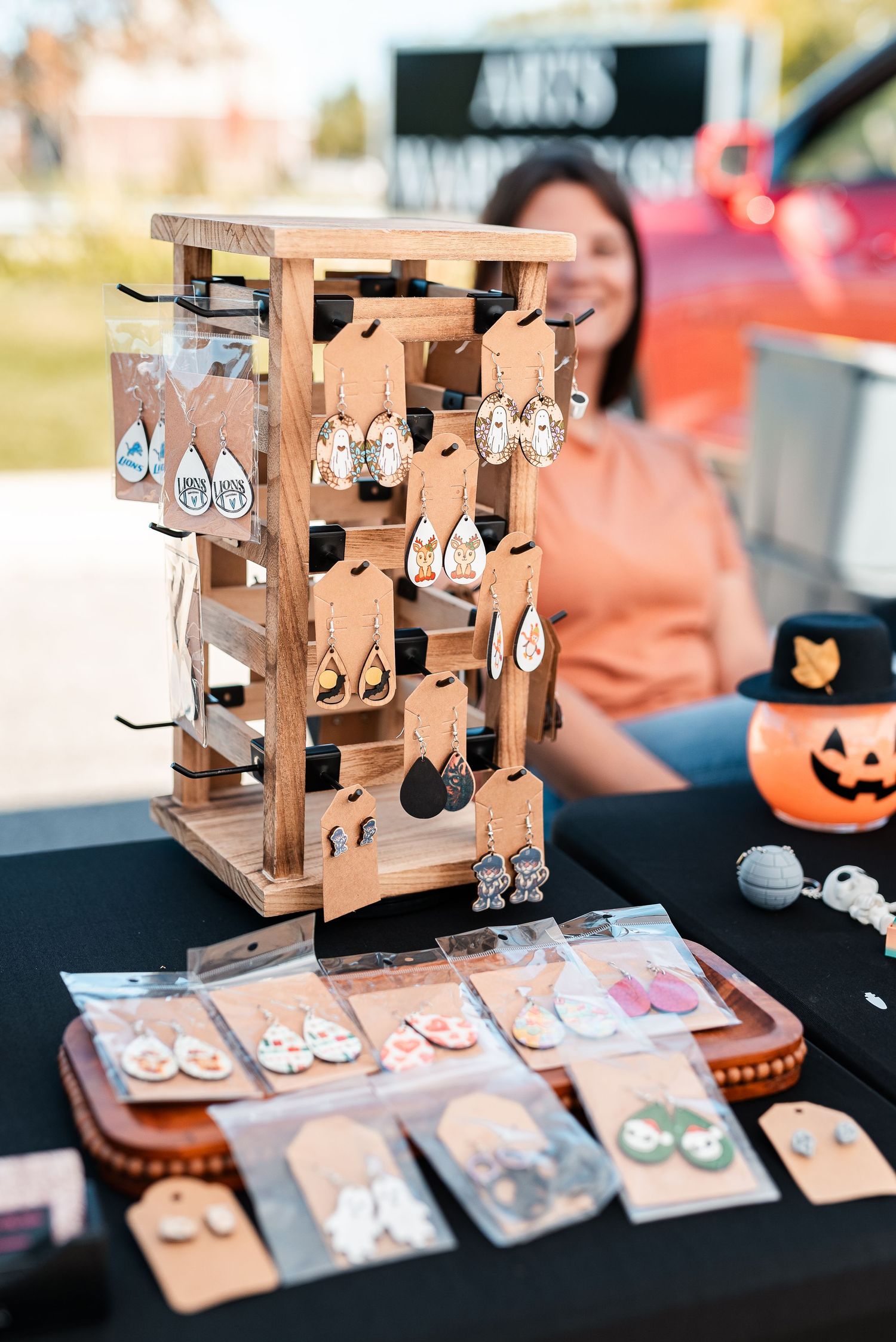 Wooden earring display stand with handmade jewelry at an outdoor fall craft market with Halloween decor.