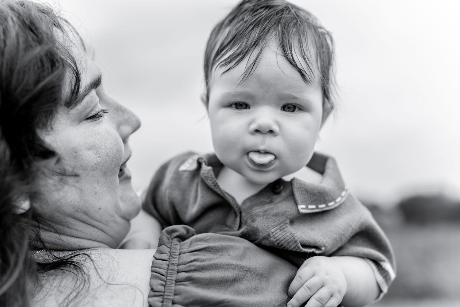 Black and white portrait of grandmother holding expressive baby sticking out tongue.