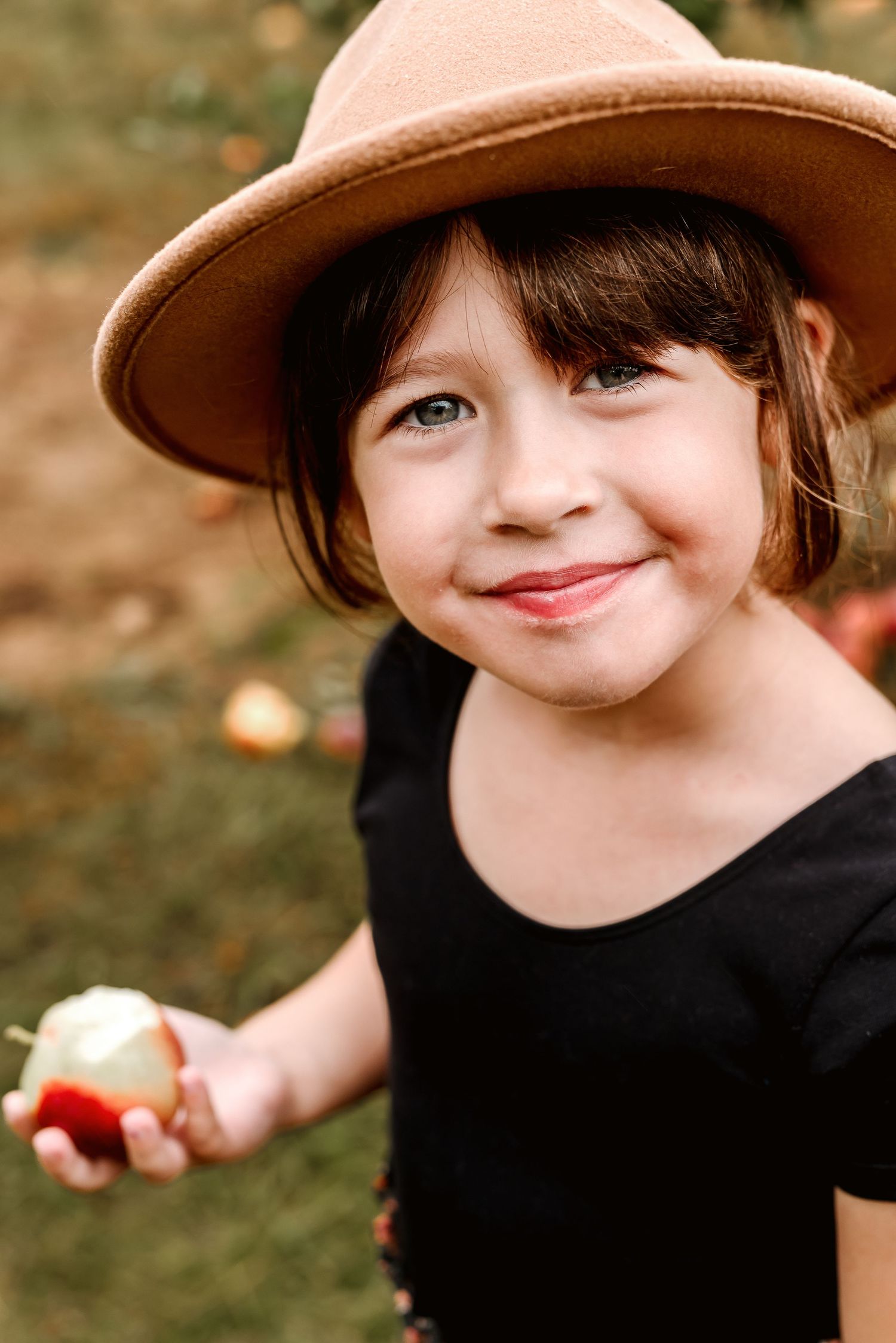 A child in a brown hat and black shirt smiles playfully in a series of candid outdoor portraits.