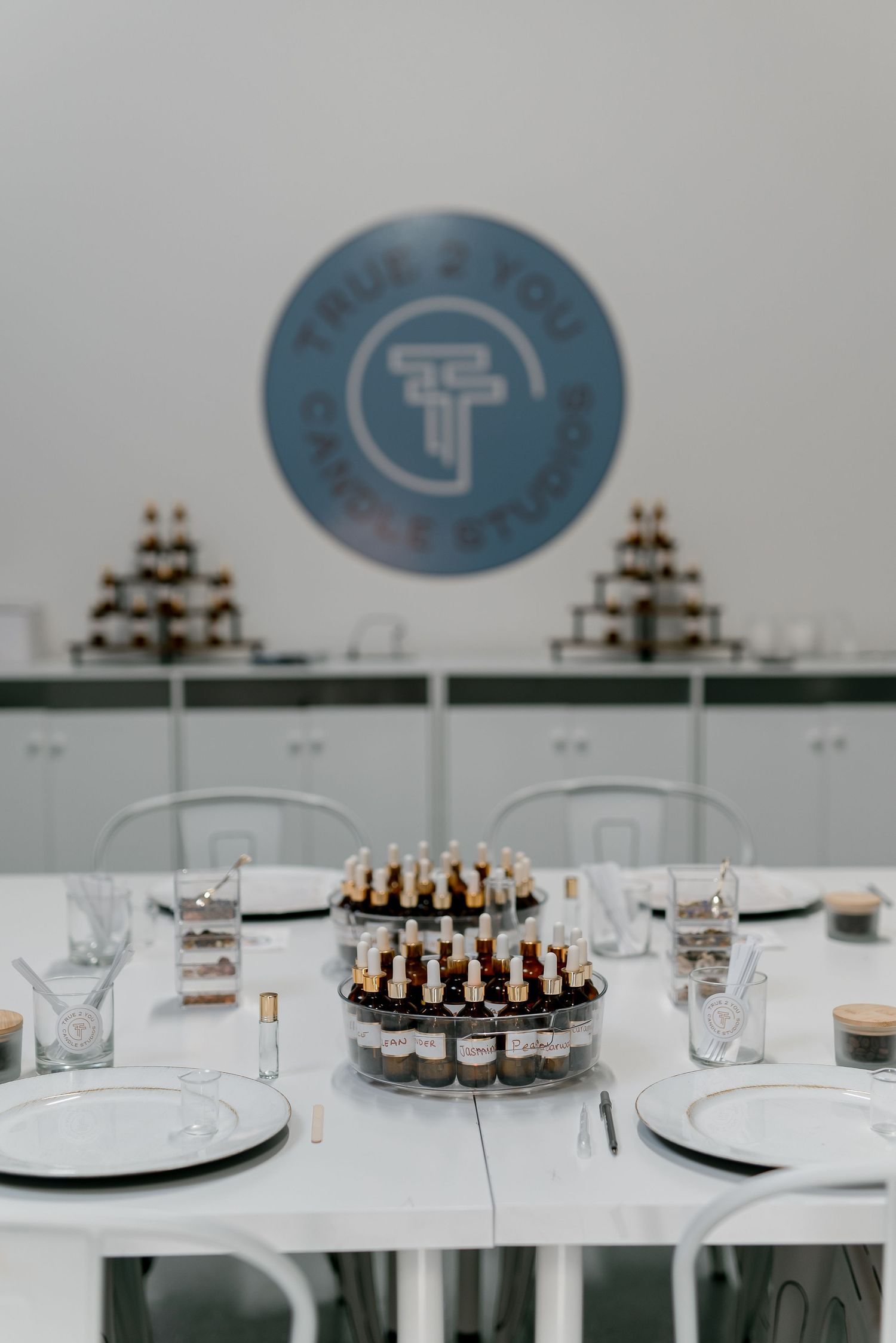 True 2 You candle studio workshop table with fragrance oils, white plates, and glassware for a candle-making class.