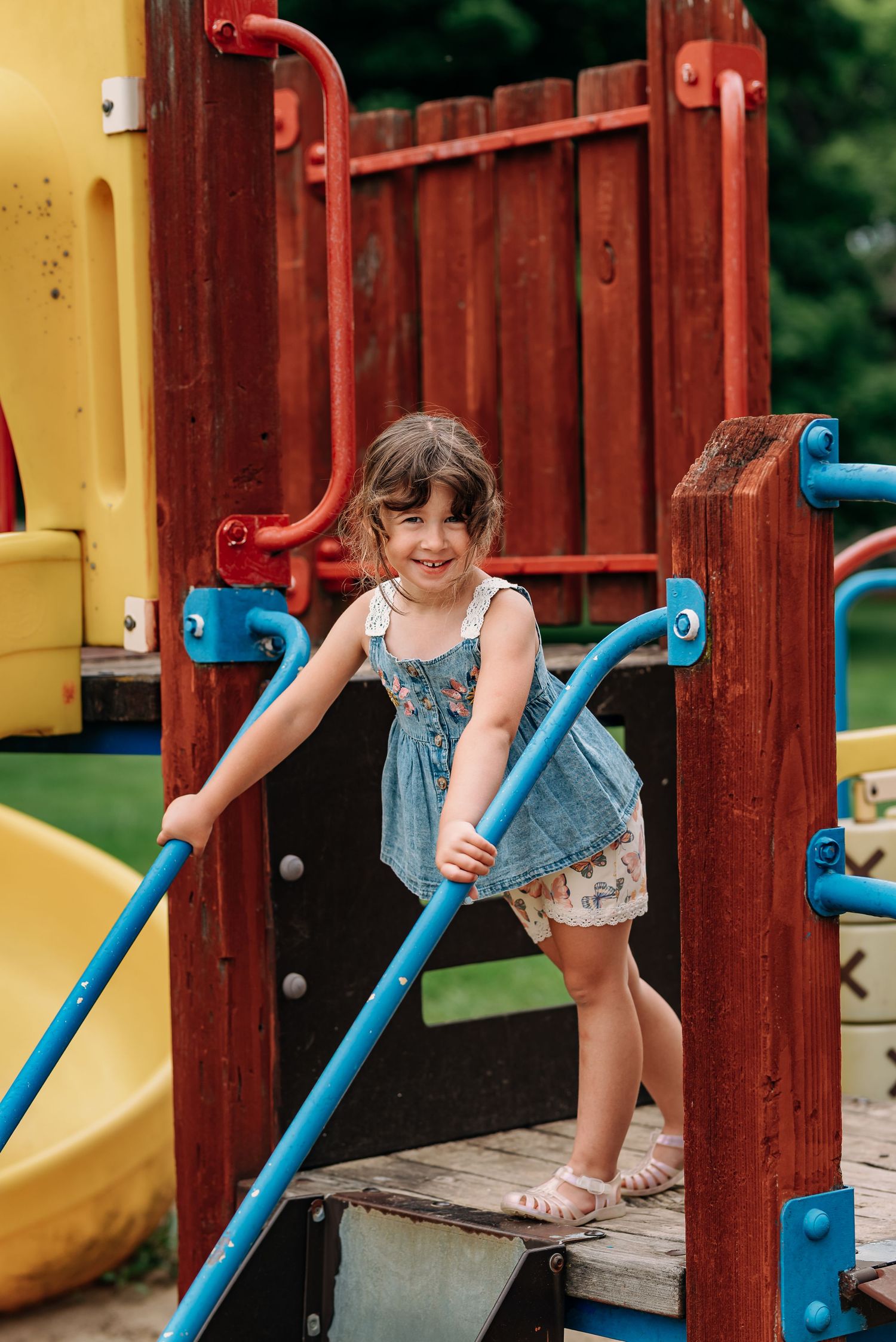 Child plays on outdoor playground equipment with blue railings and wooden structures.