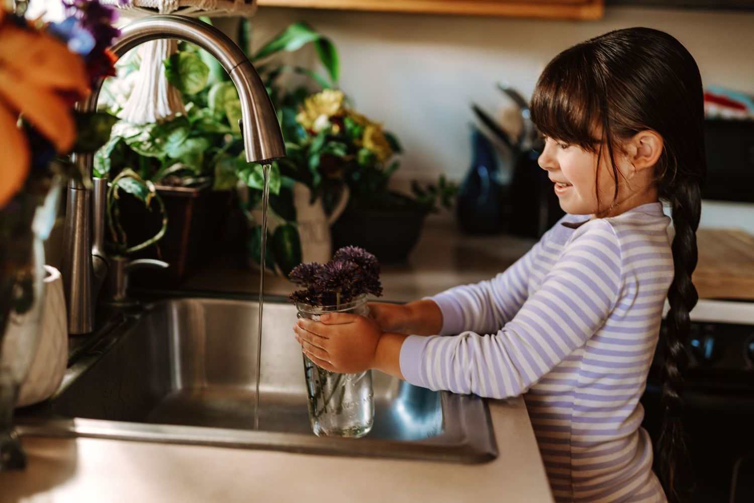 A sequence of images showing someone watering houseplants in a kitchen window with a glass jar.