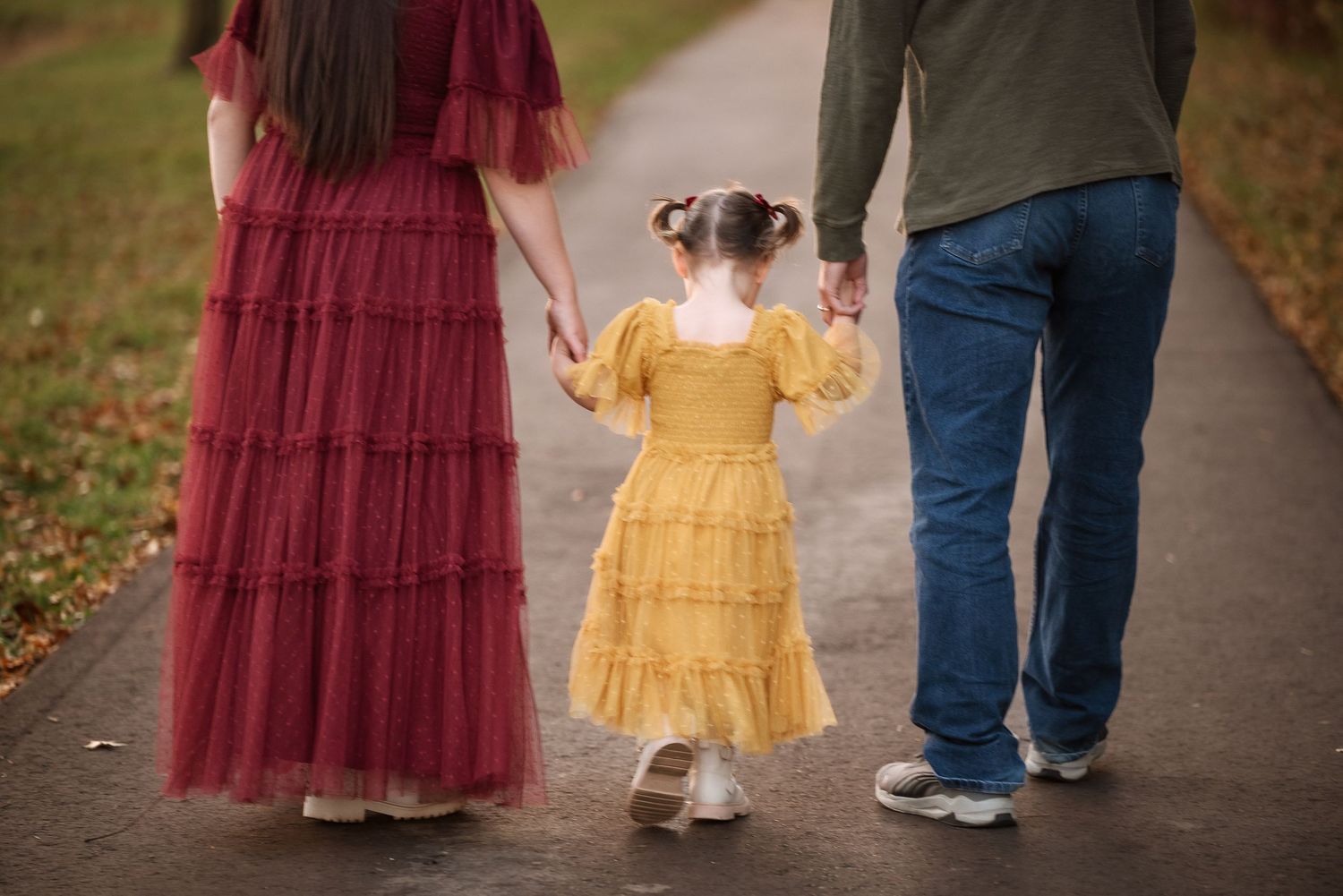 A close-up view of feet walking on a path shows burgundy dress and blue jeans with white sneakers.