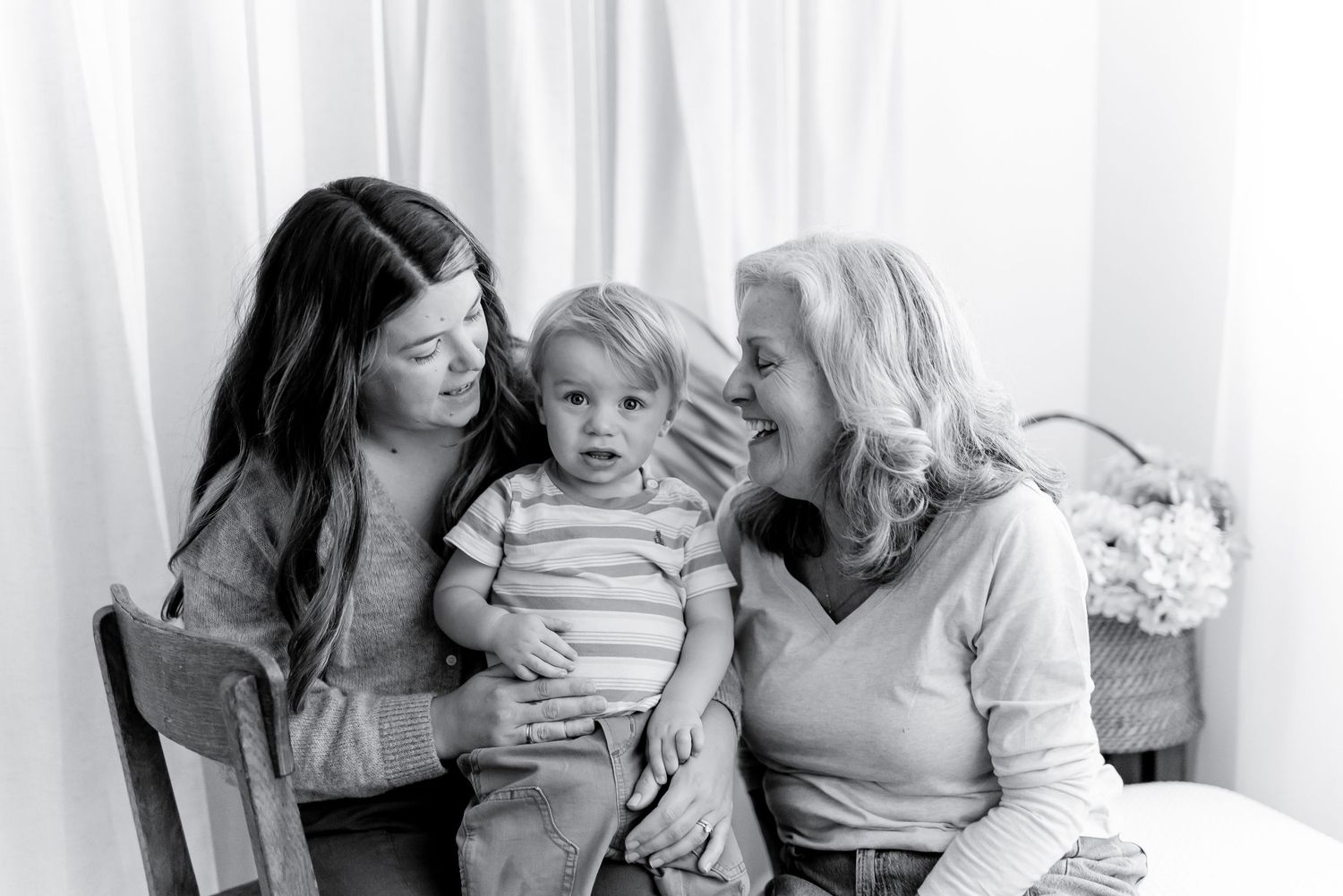 Black and white portrait of a young woman, a smiling older woman, and a toddler sitting close together in a bright, softly lit room.