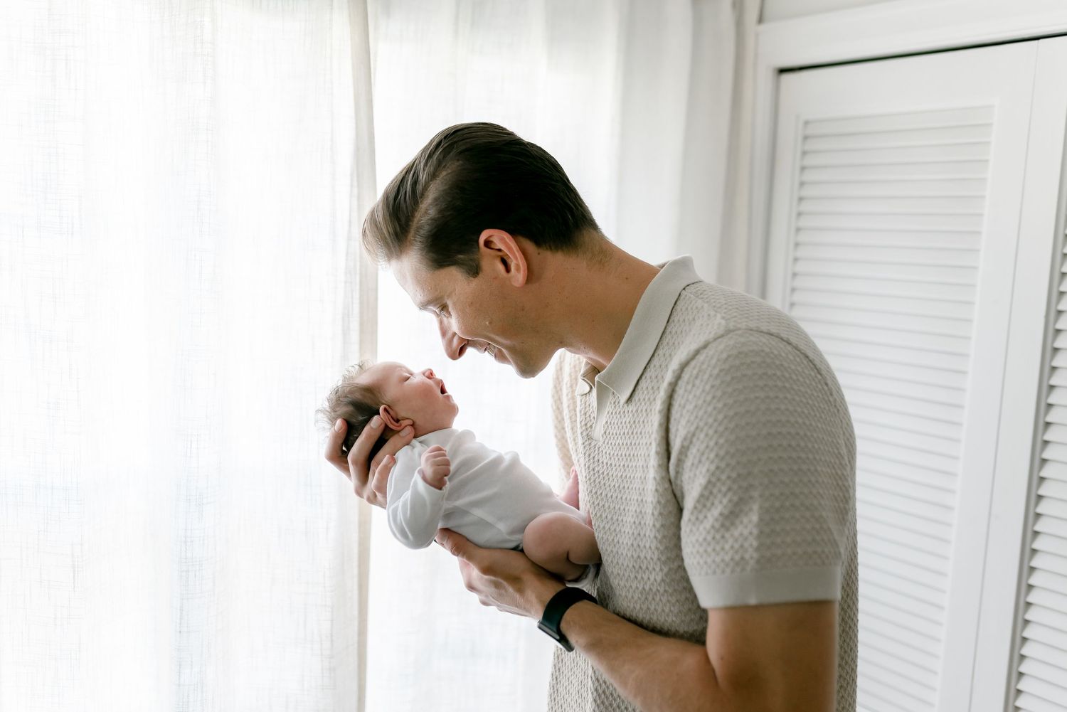 A father tenderly holds his newborn baby near a bright window, sharing a precious bonding moment.