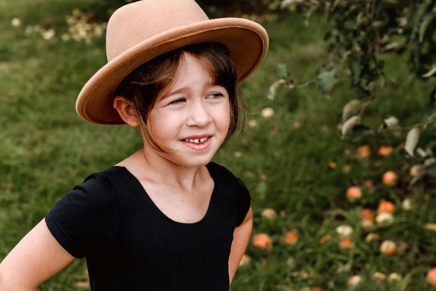 A brown hat rests on a person's head against a green background with orange pumpkins visible in the distance.
