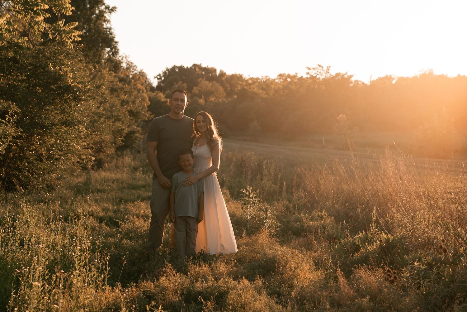 Couple embracing at golden hour in a sunlit meadow surrounded by trees in a romantic outdoor setting.