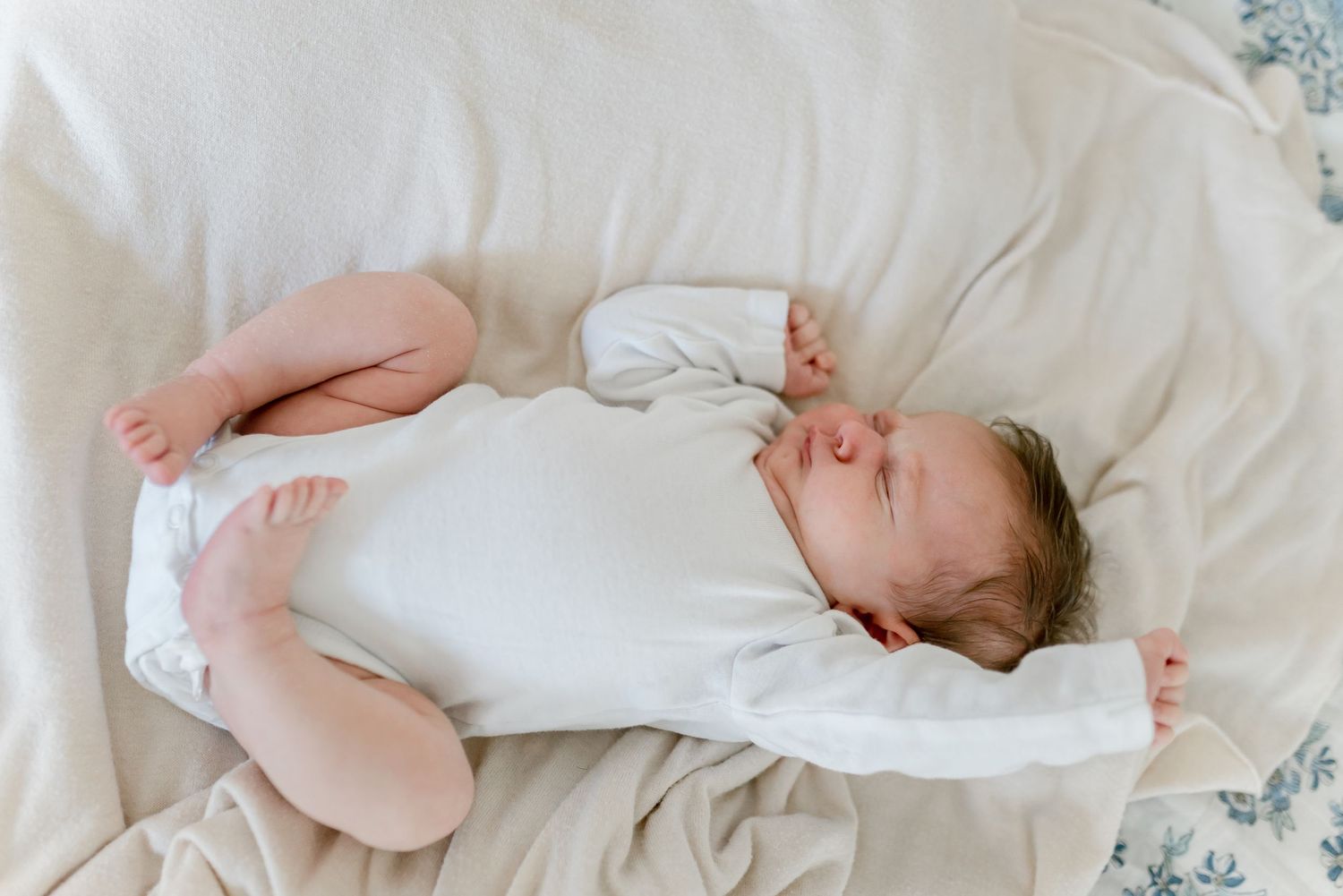 Peaceful newborn baby sleeping in white onesie on soft cream bedding.