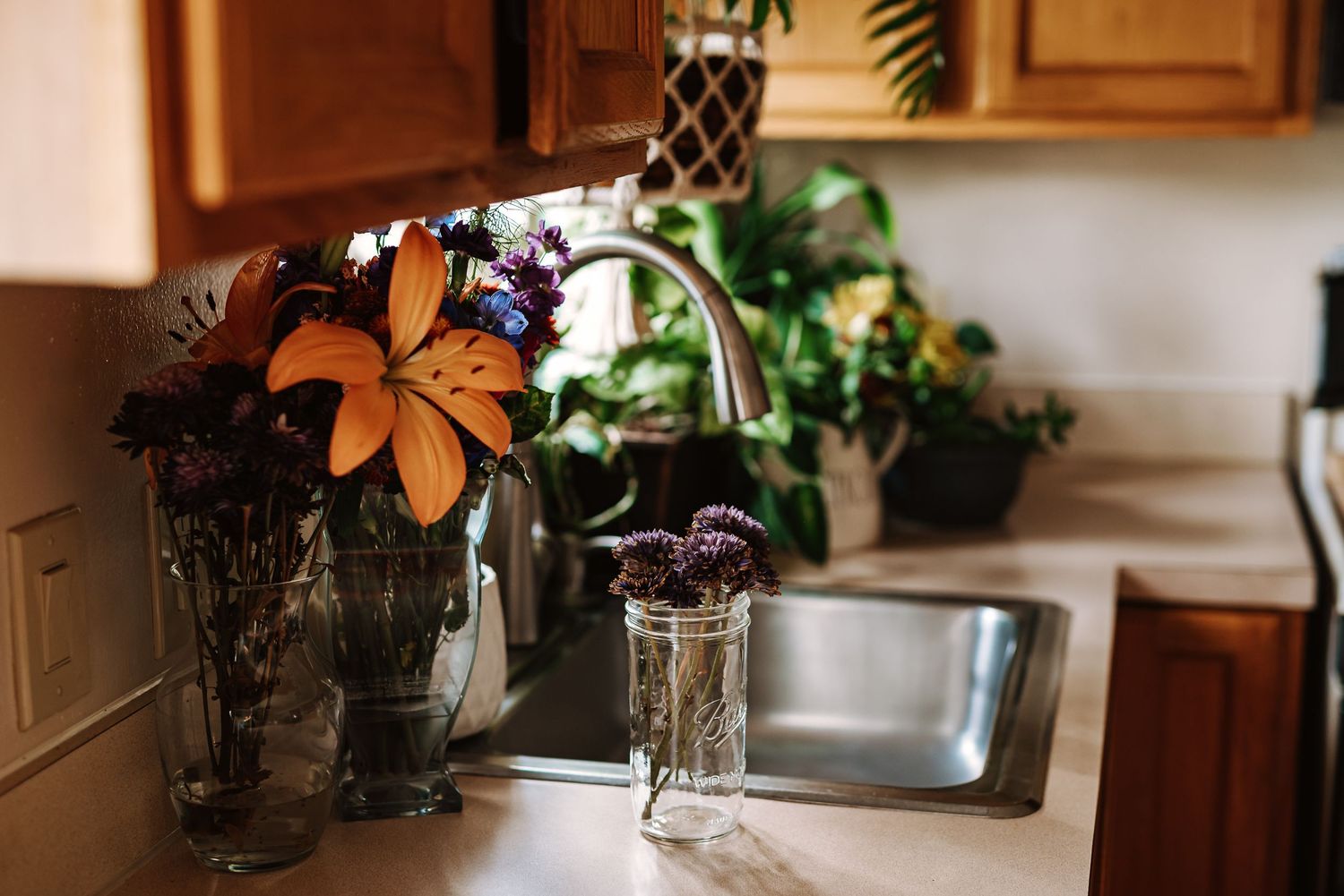 A rustic kitchen counter with mason jars and orange flowers arranged near wooden cabinets in warm lighting.