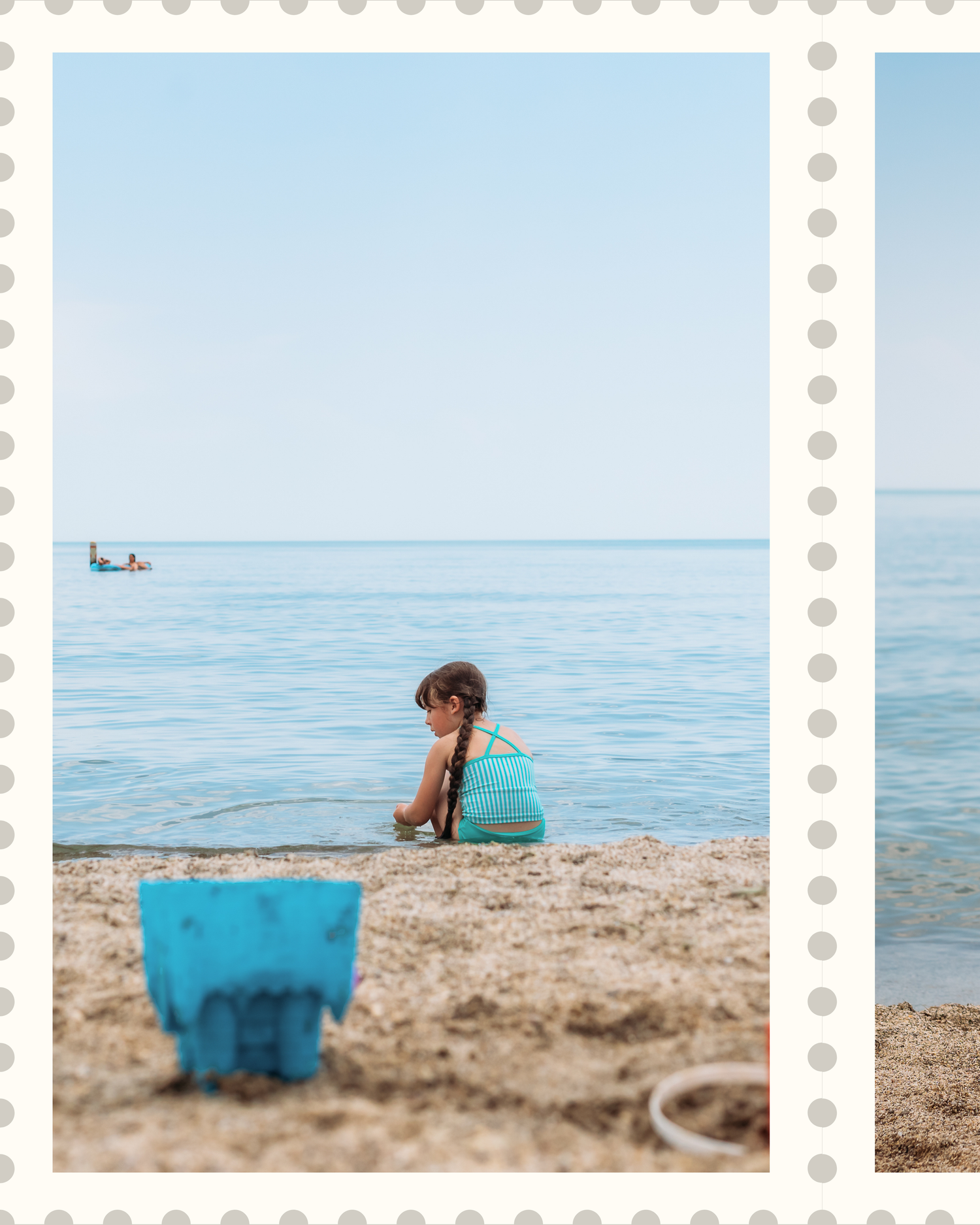 Someone in turquoise swimwear sits on a sandy beach looking out at the calm blue ocean with a blue bucket nearby.