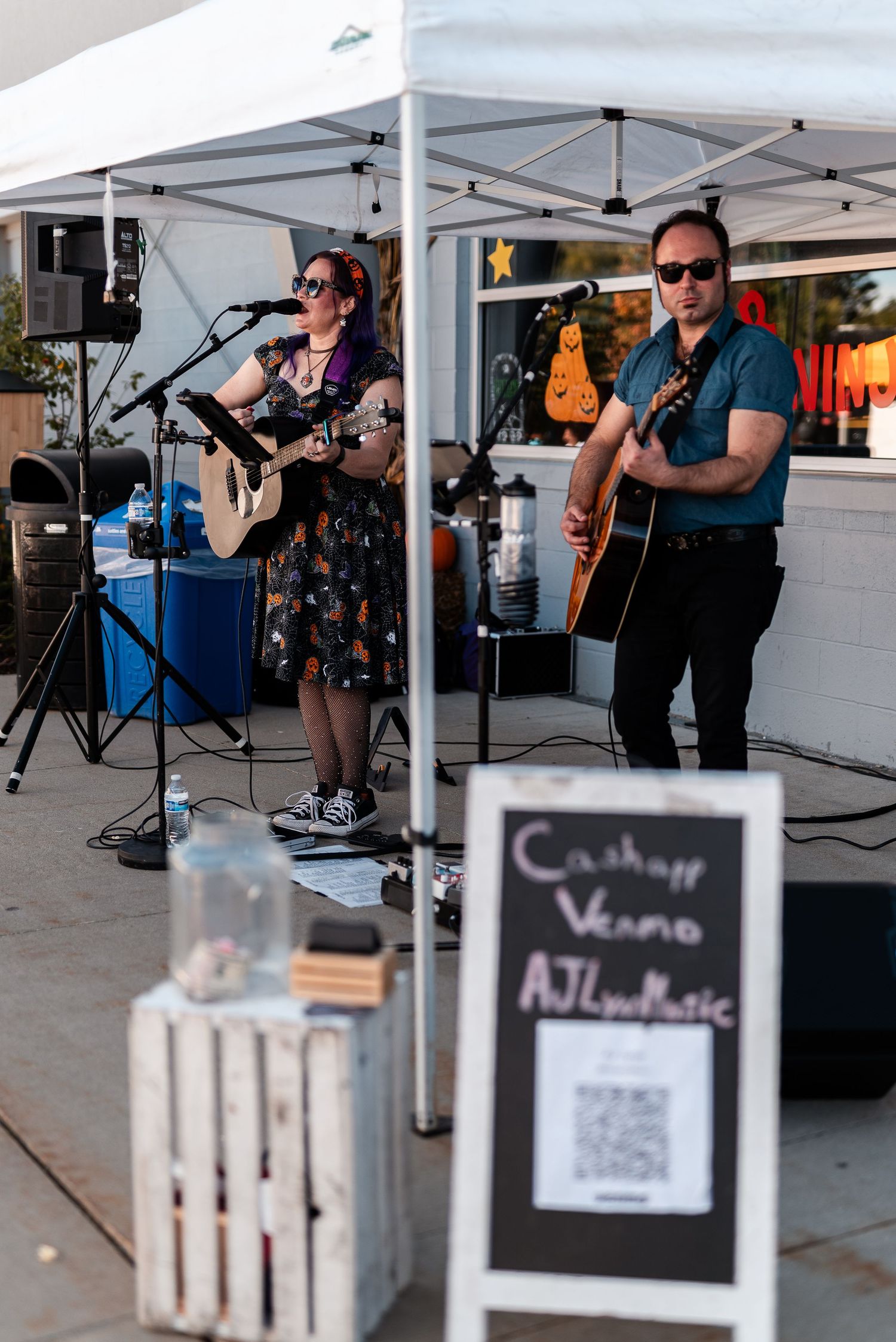 Two guitarists perform live acoustic music outdoors under a tent with a Cashapp Venmo AJLynMusic sign.