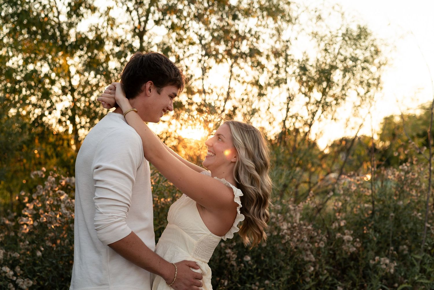Couple embracing at golden hour sunset in a wildflower field, sharing a romantic moment outdoors.