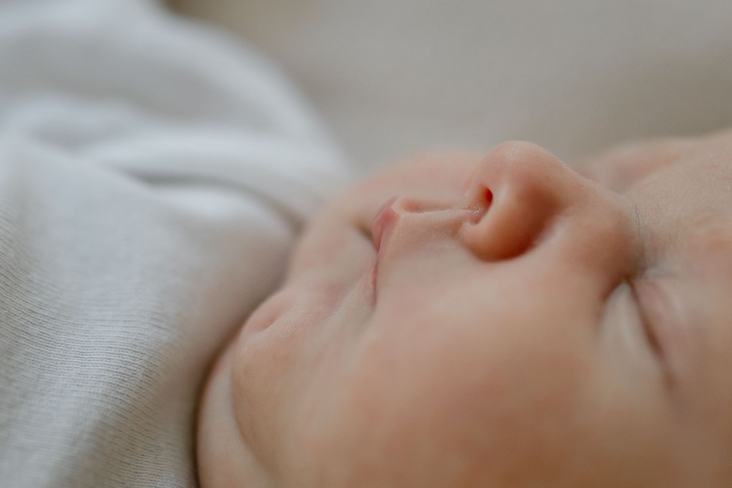 Close-up of a sleeping newborn baby's face and tiny hands wrapped in a soft white blanket.