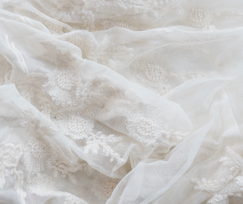 Delicate white lace fabric with embroidered floral patterns creates soft folds and romantic texture.