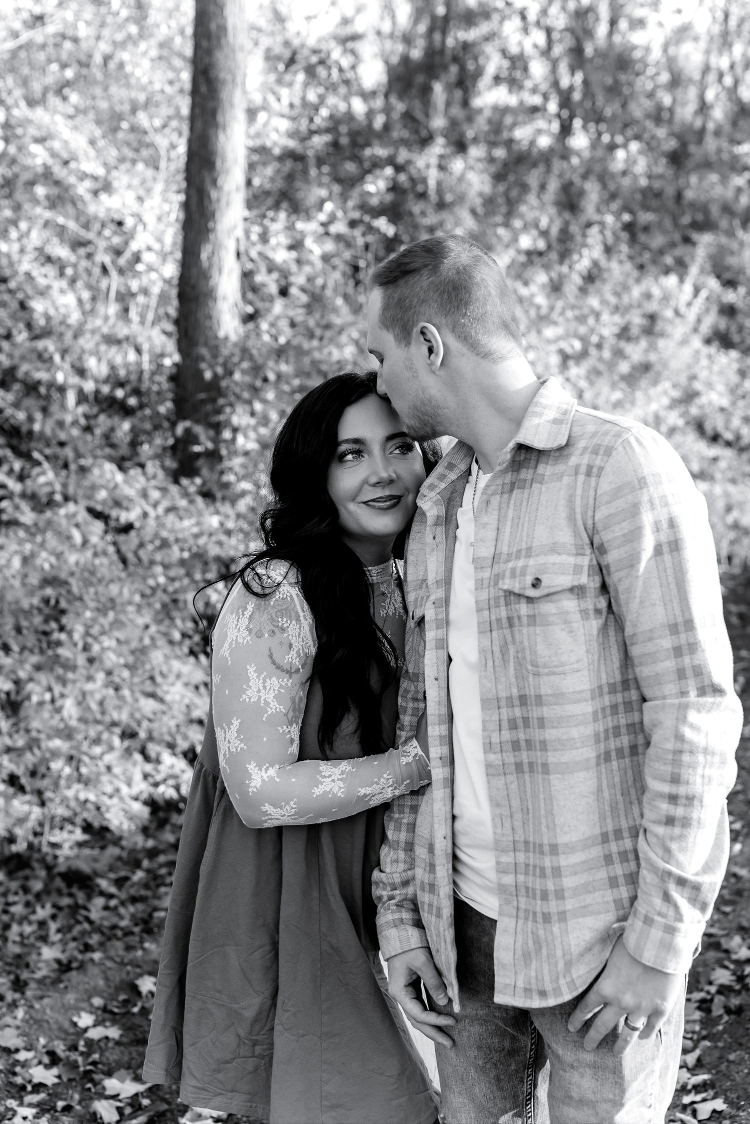 A romantic couple shares tender moments in a series of black and white photos taken outdoors in a wooded setting.