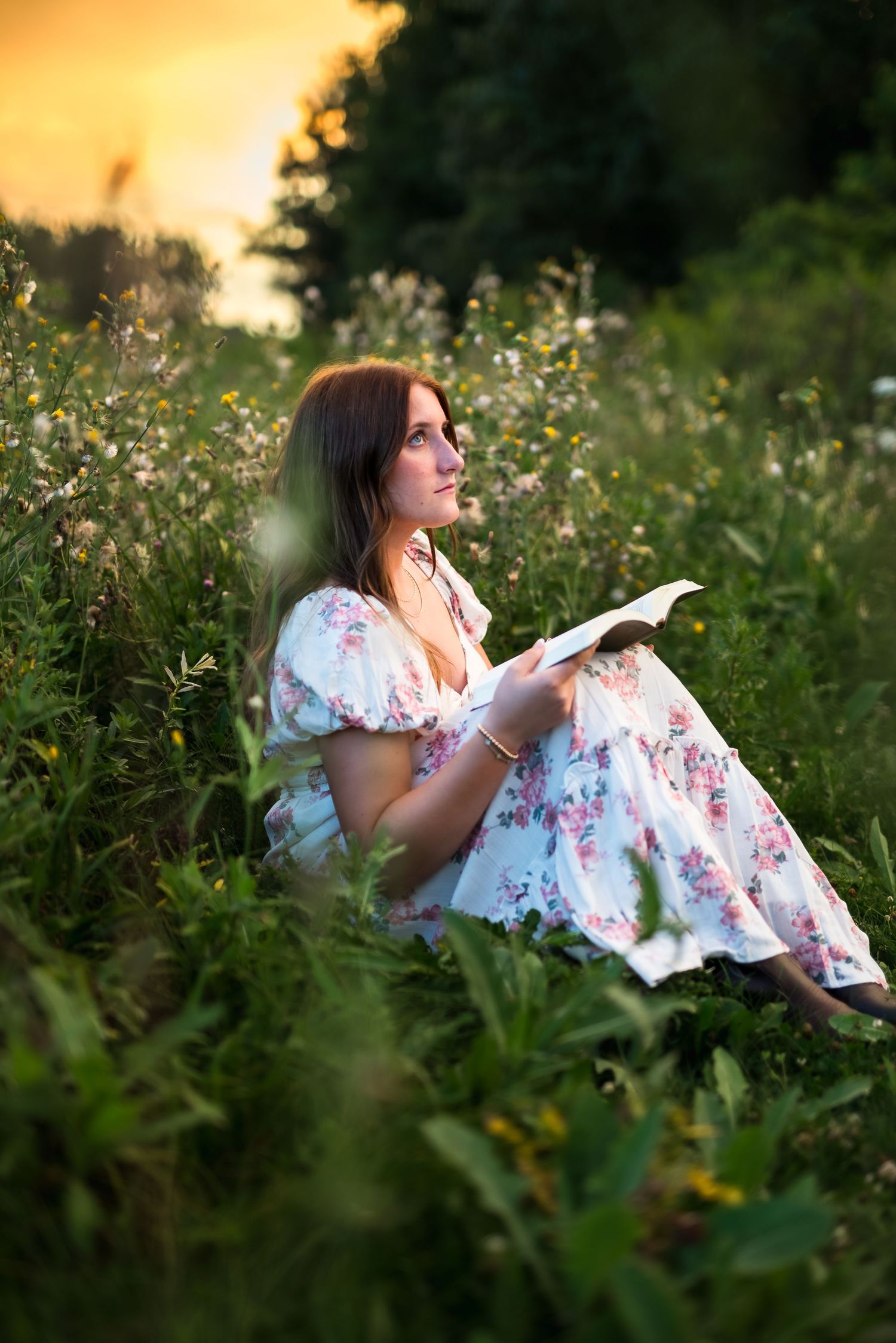 Someone in a floral dress reads a book while relaxing in a wildflower meadow at sunset.