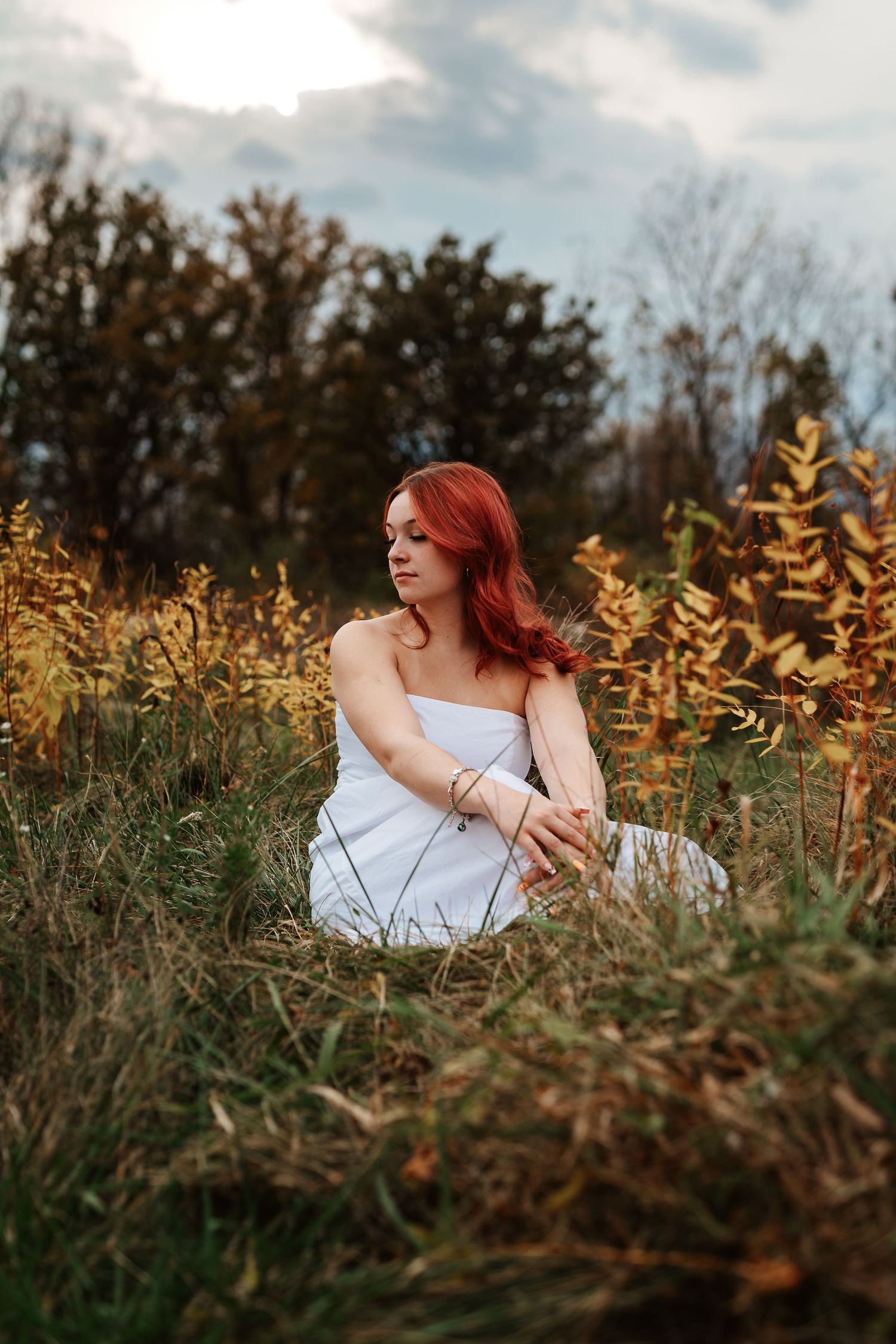 A woman in a white dress sits gracefully among golden wheat fields at sunset creating a dreamy outdoor portrait.