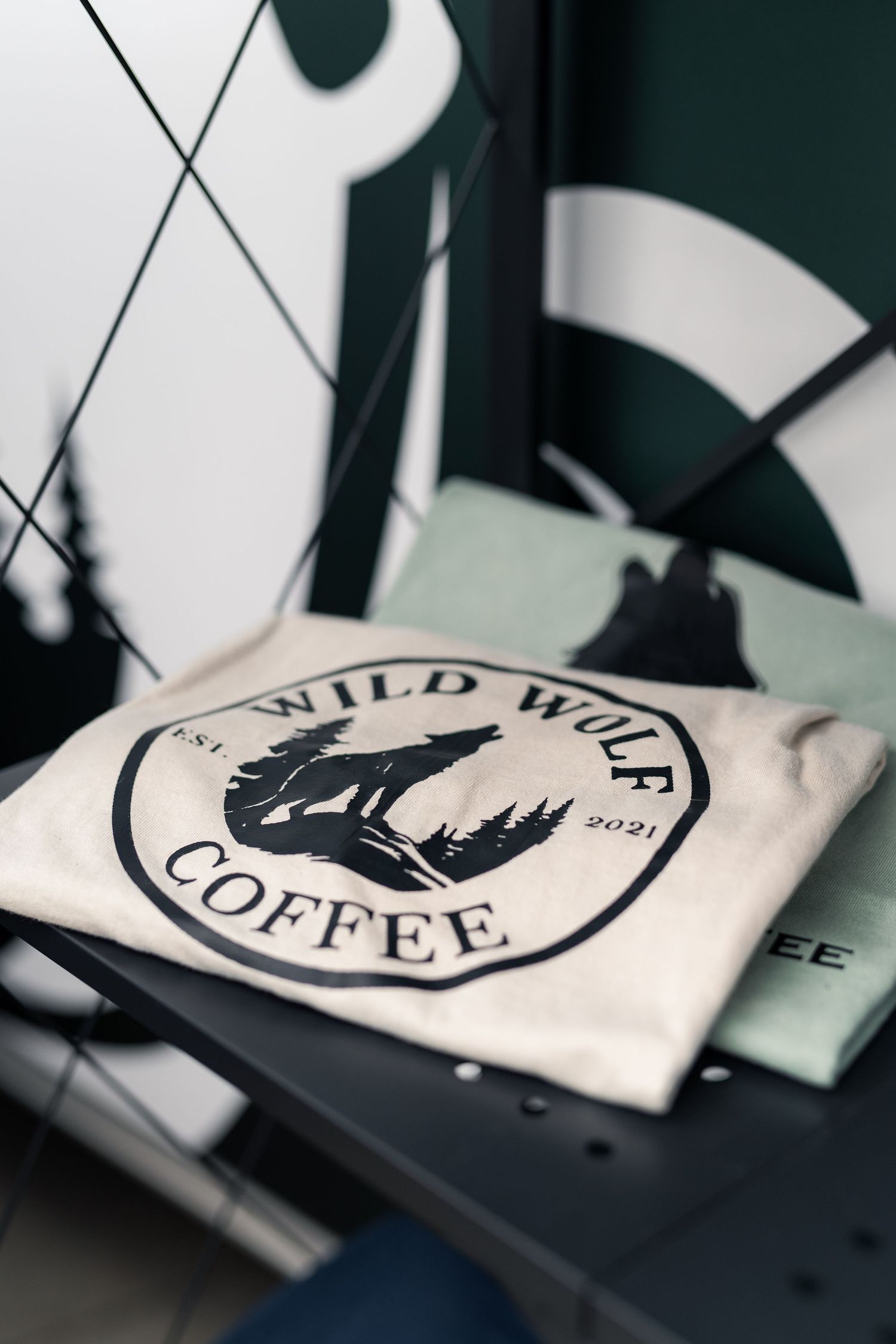 Folded white Wild Wolf Coffee t-shirt with circular wolf logo, established 2021, displayed on a black metal shelf.