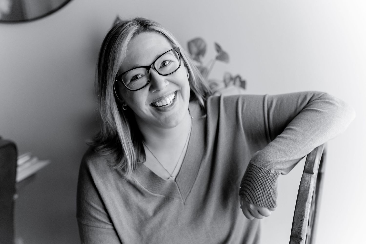 Smiling woman with glasses and blonde hair laughing in a black and white portrait photo.
