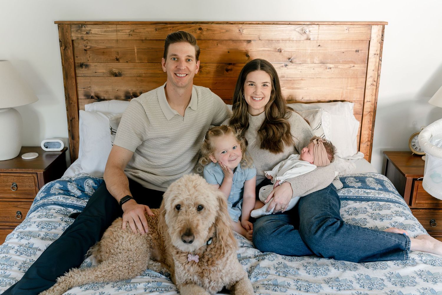 Happy family with two children and a golden doodle dog posing together on a bed with floral bedding.