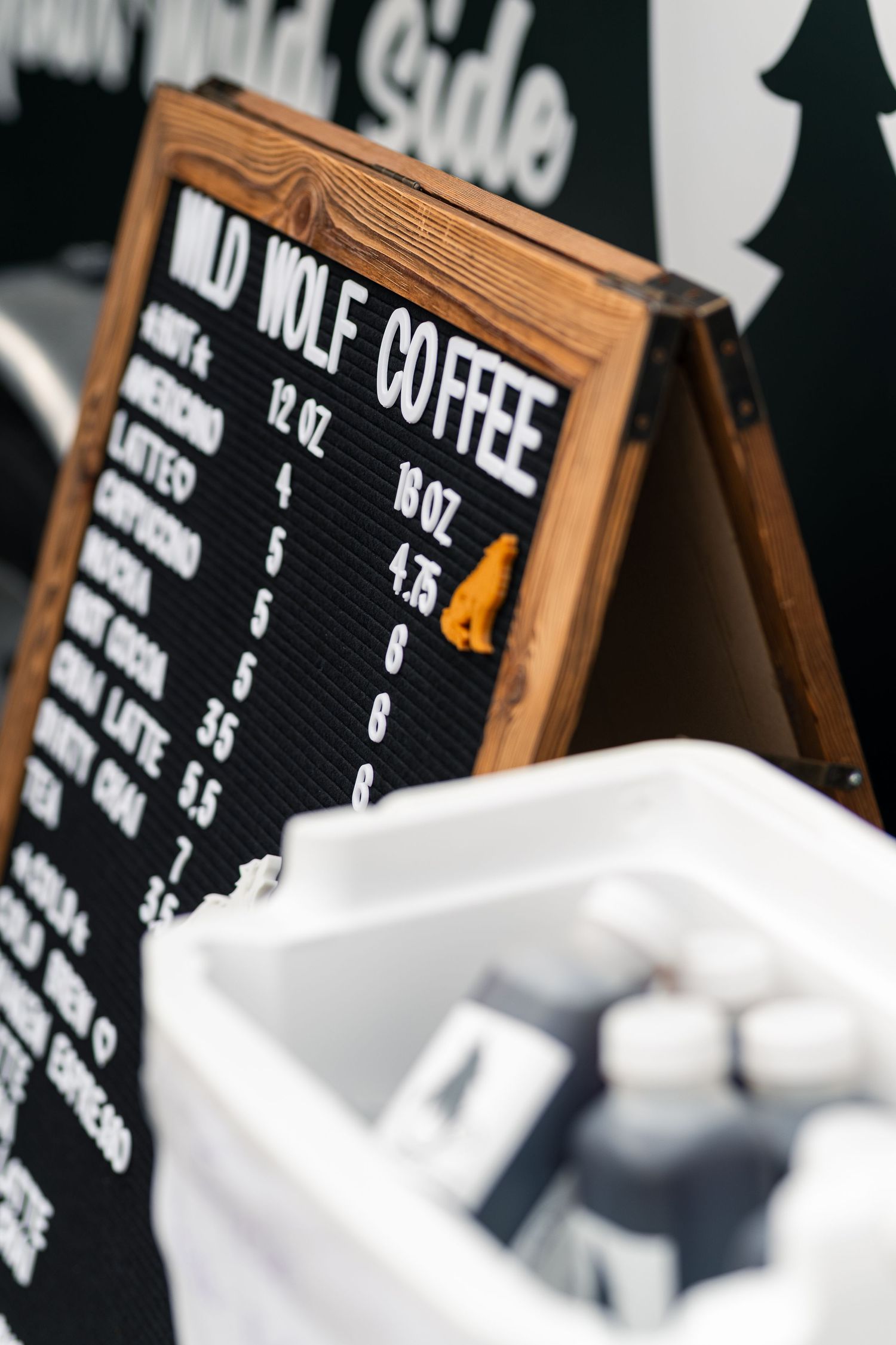 Wild Wolf Coffee menu board displaying drink sizes and prices, displayed outdoors at a market or pop-up event.