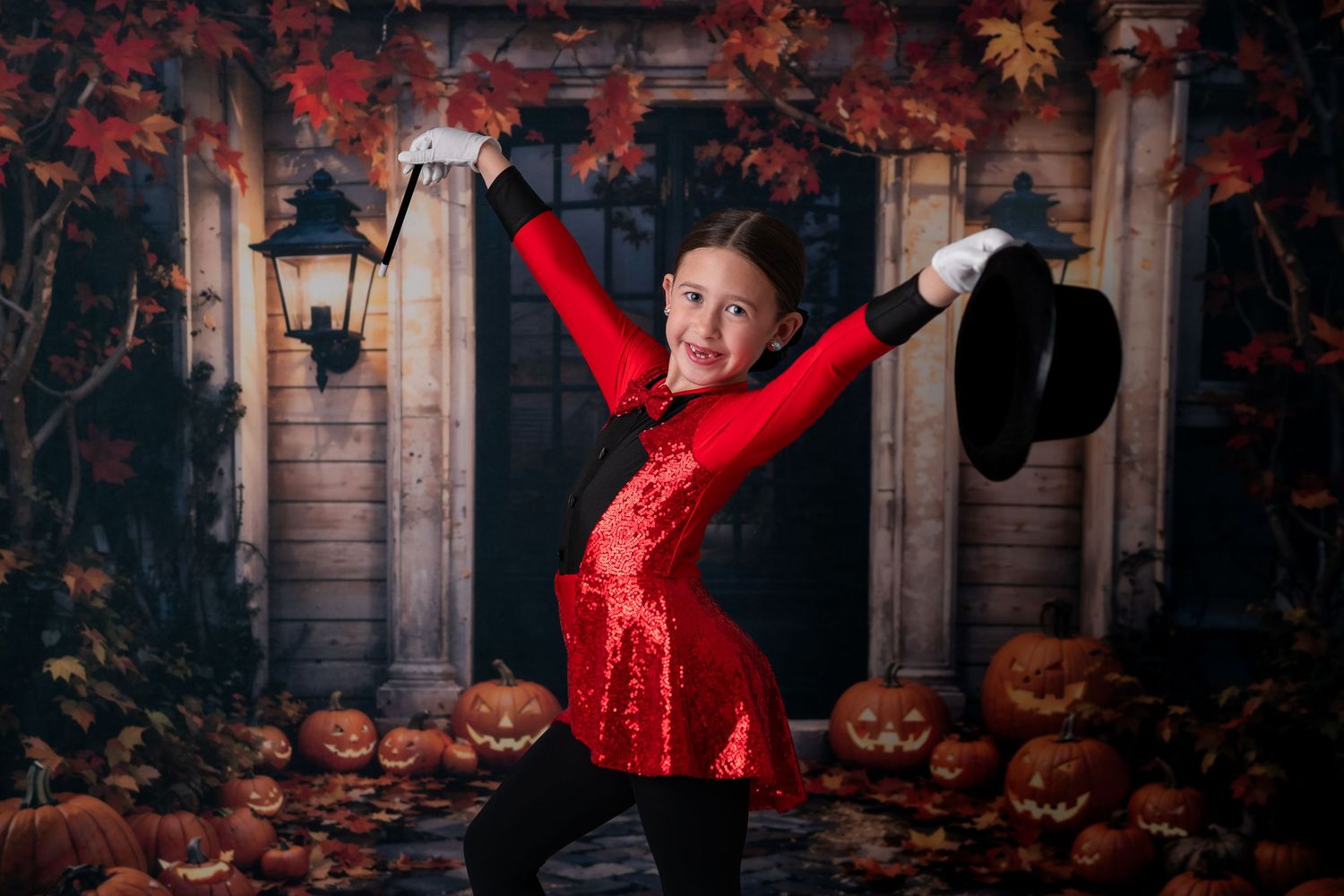 Girl in red sequin magician costume poses with top hat among Halloween pumpkins and autumn leaves backdrop.