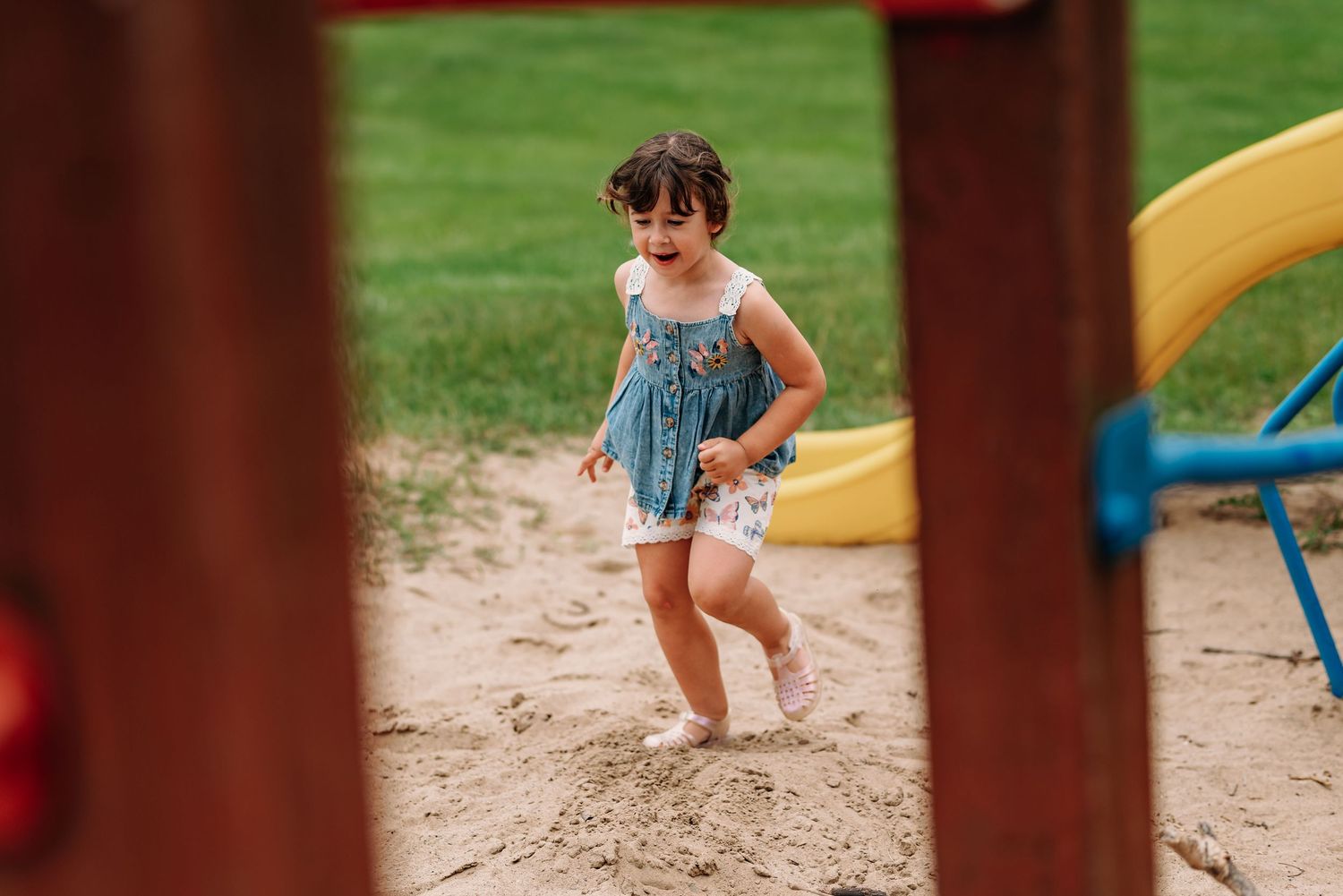 Child playing and running through a wooden playground structure on a sunny day outdoors.