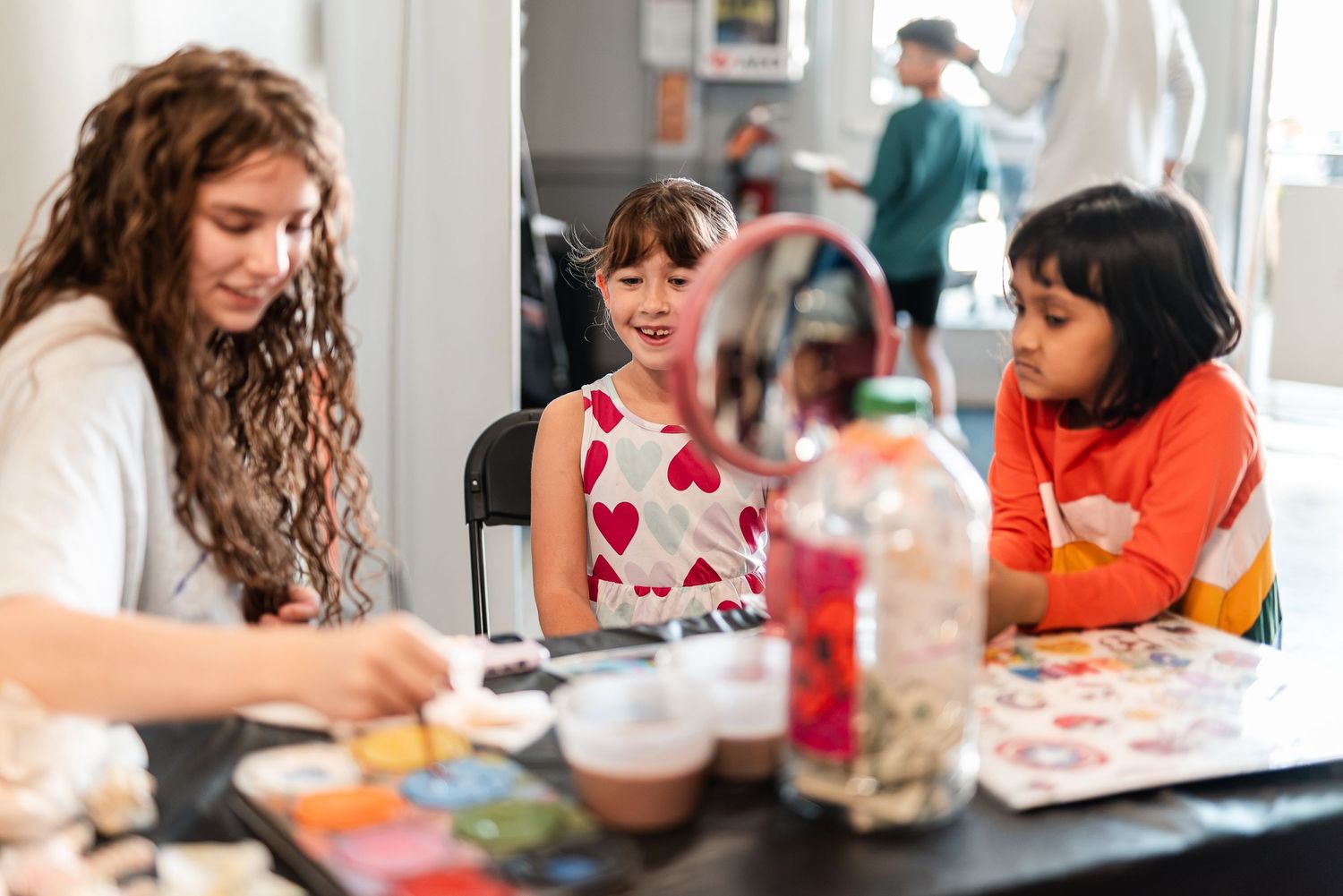 Woman and two young girls engaged in a creative craft activity at an indoor art table.