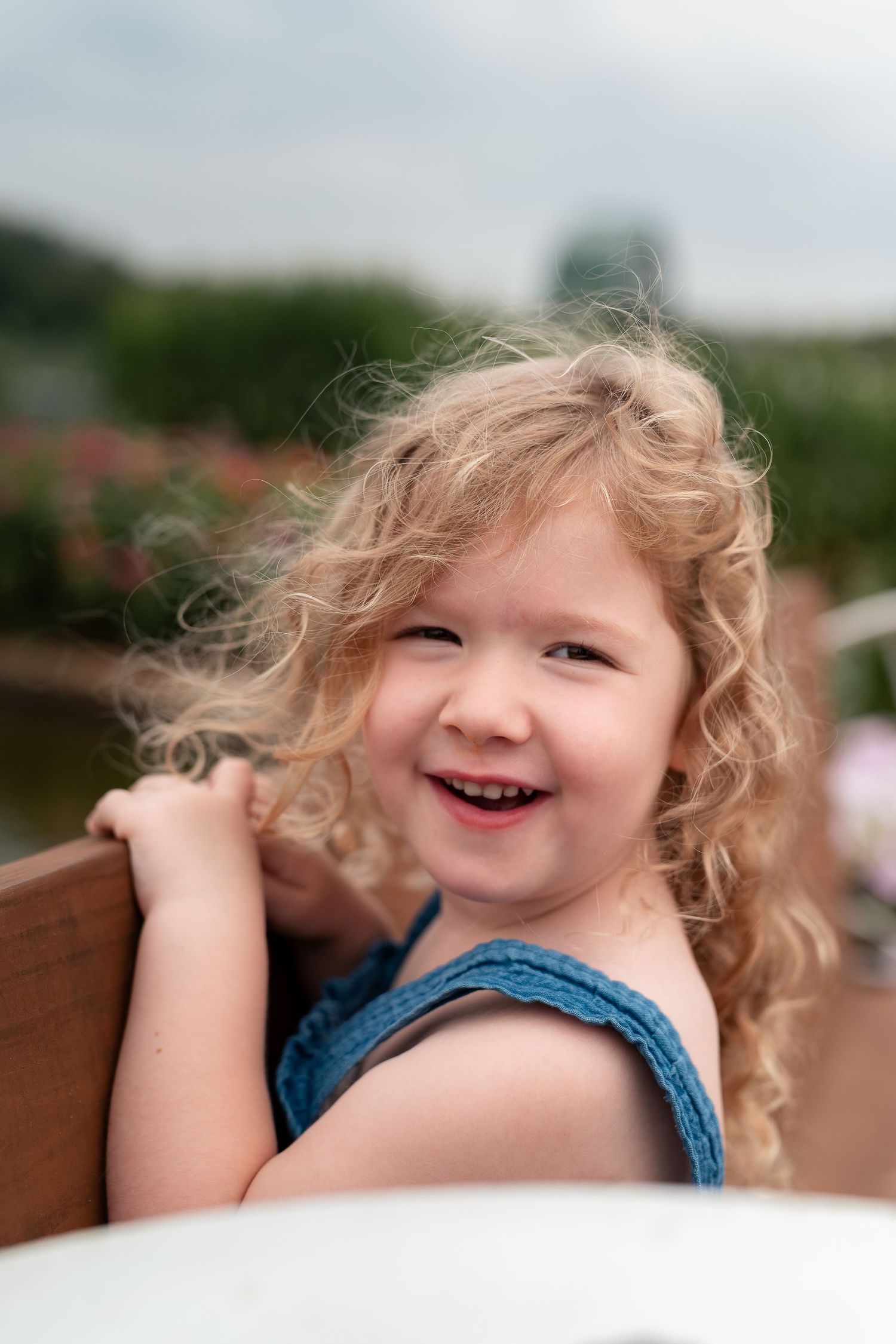 Happy curly-haired little girl laughing outdoors in a blue dress.