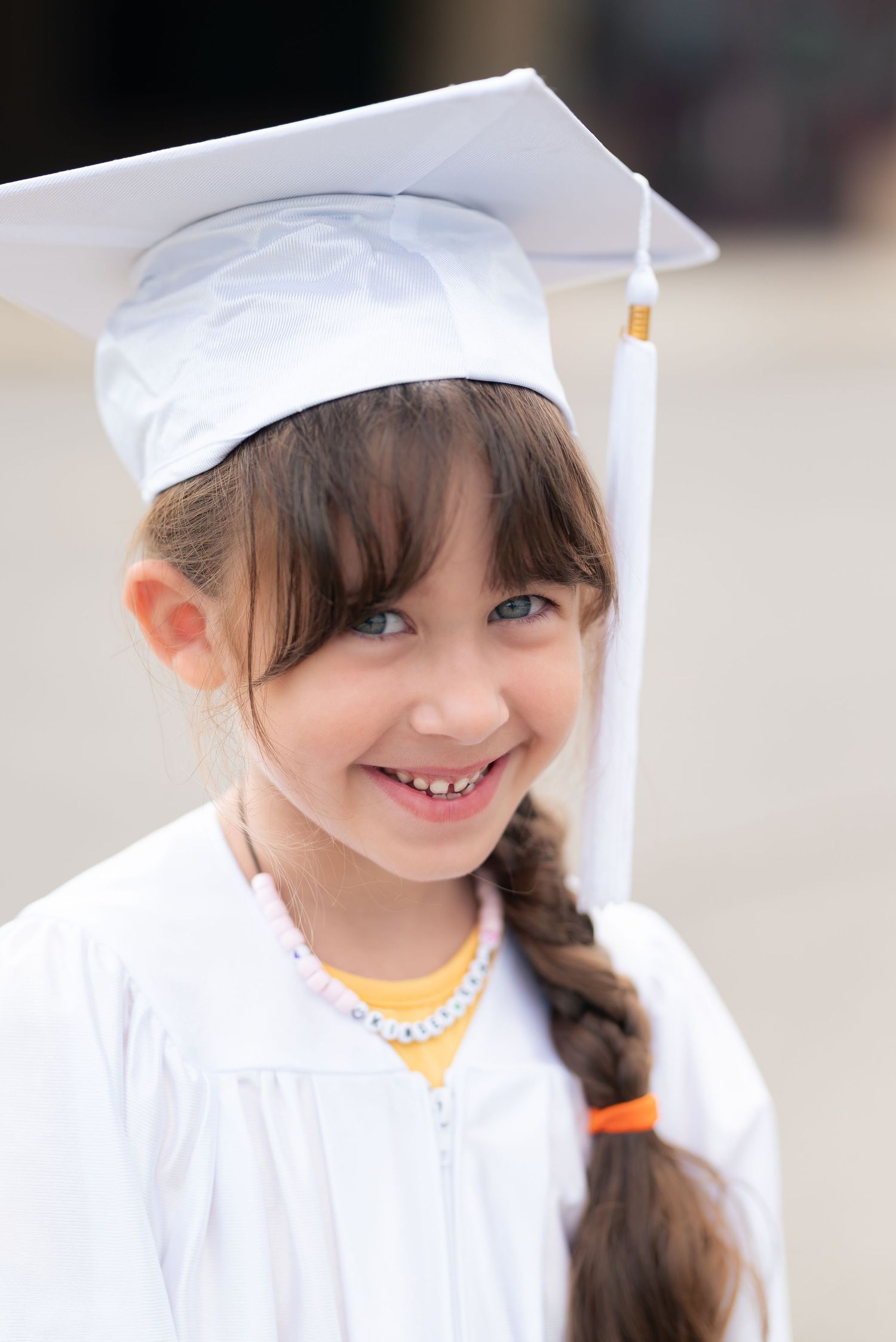 A child in white graduation cap and gown smiles brightly during a graduation ceremony.