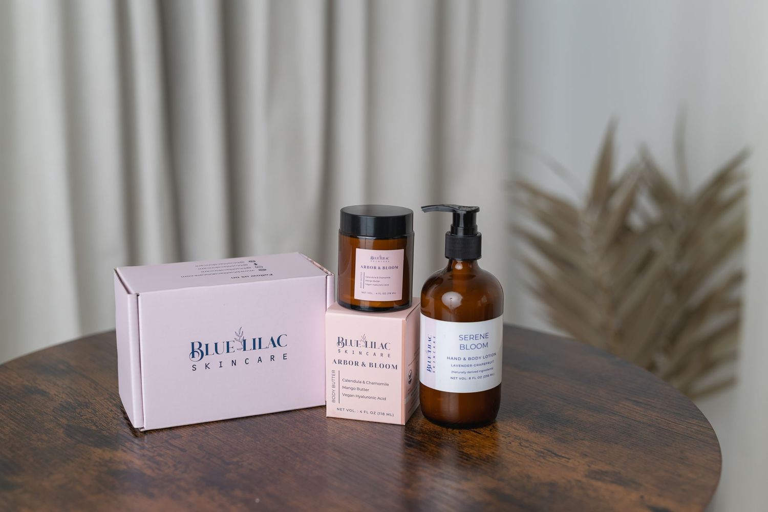 Blue Lilac Skincare gift set with pink box, amber glass candle and pump bottle on wooden table.