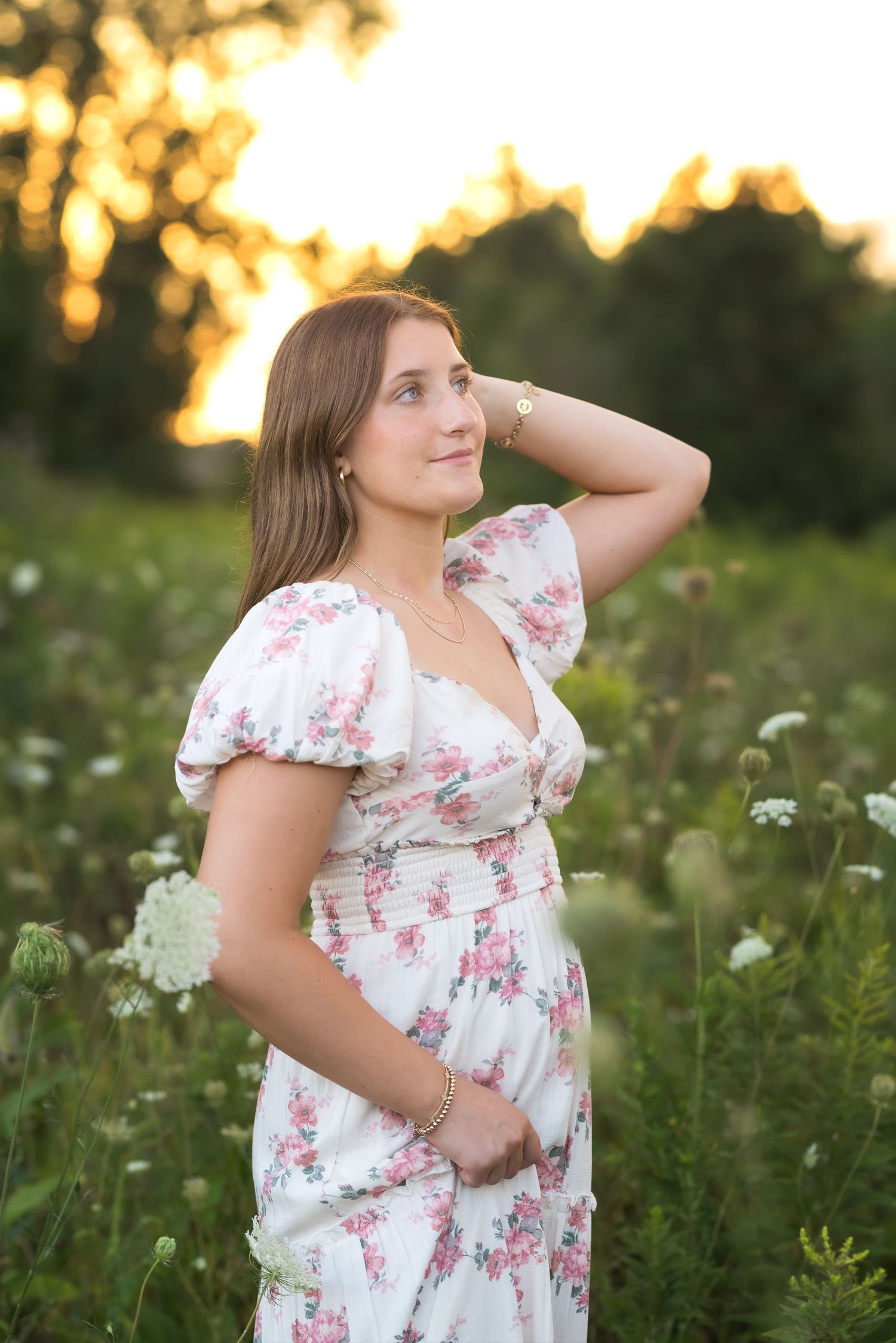 A person in a floral dress poses gracefully in a wildflower field at sunset.