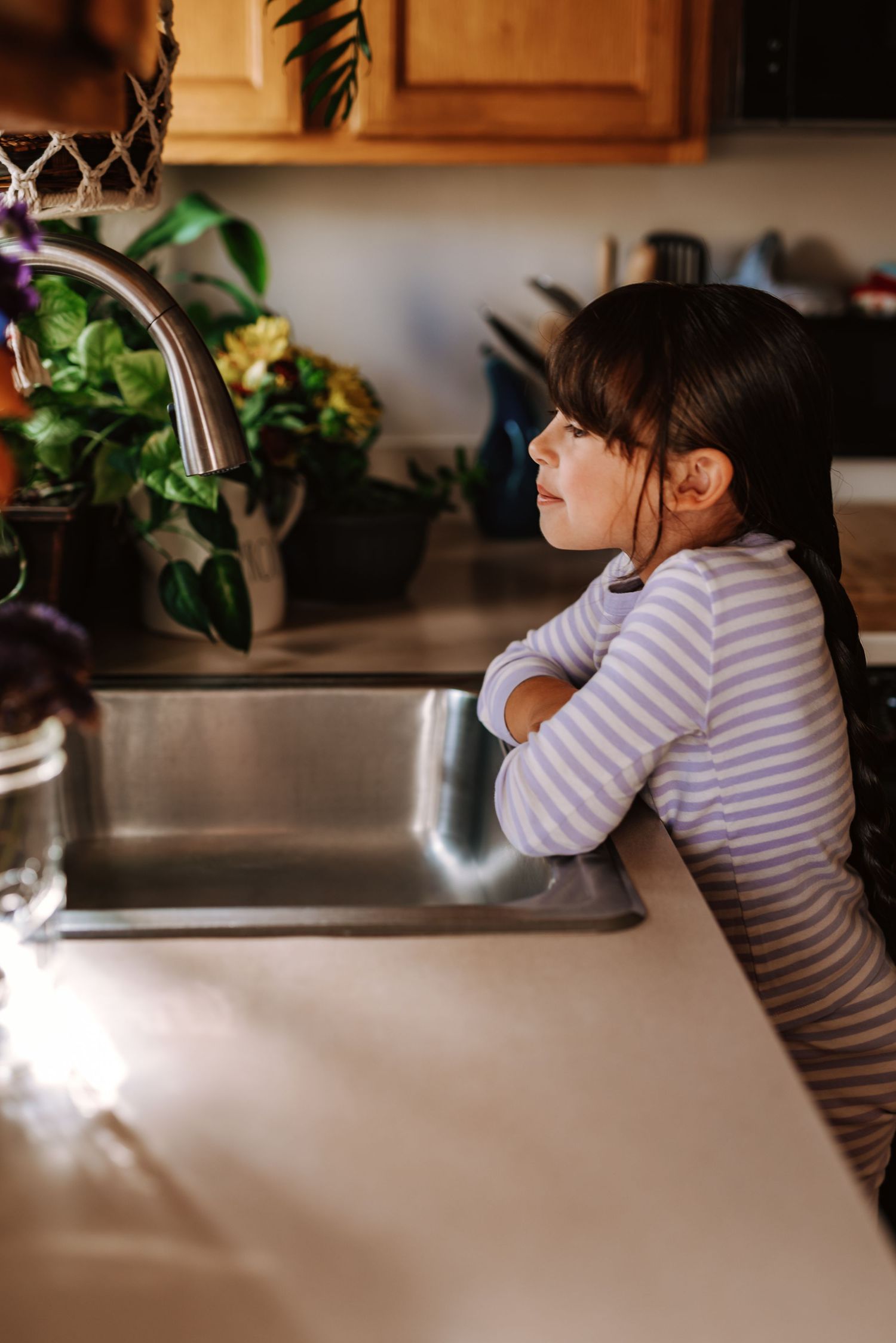 A person in a striped shirt sips a hot beverage while sitting at a counter with houseplants in the background.