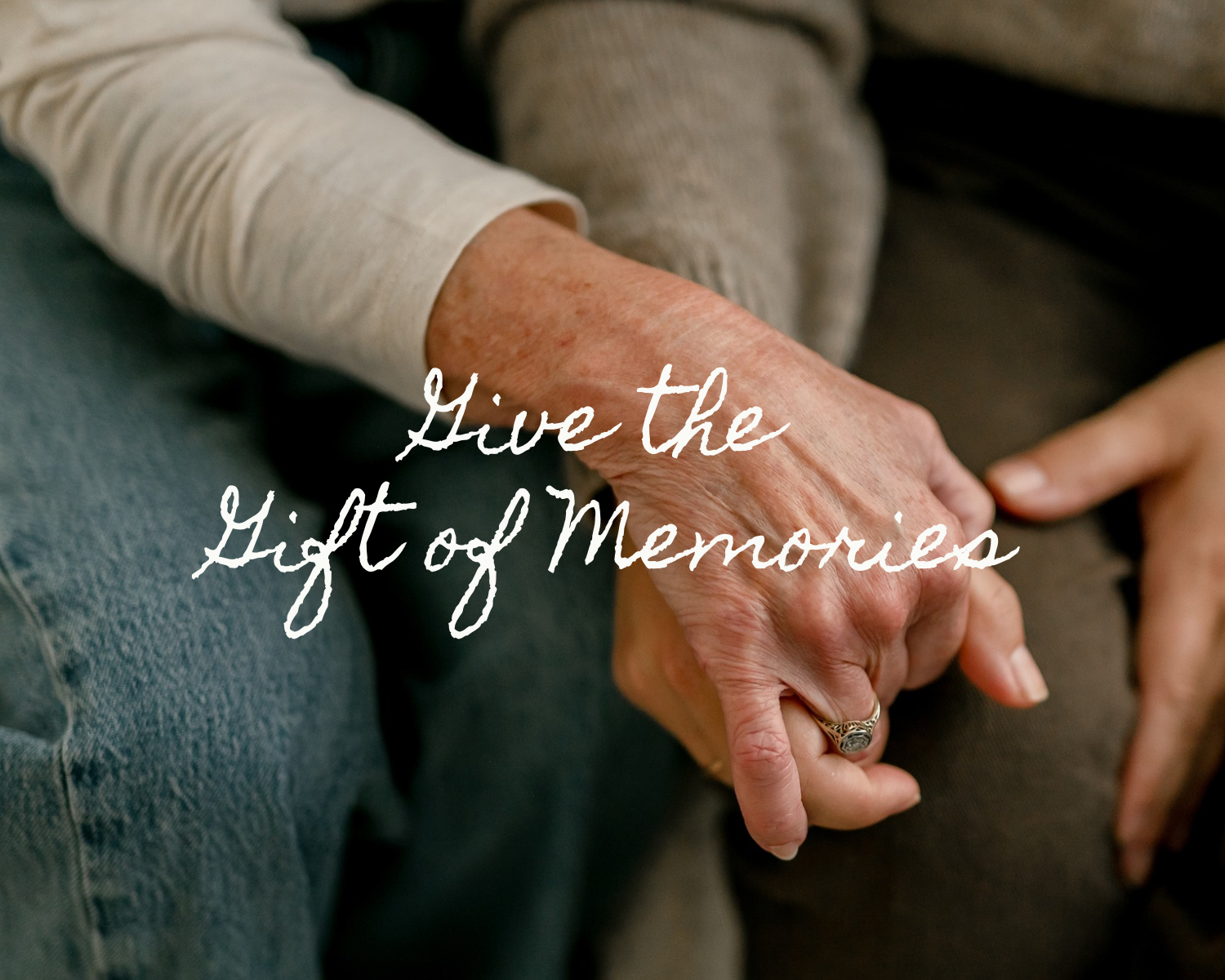 Two elderly hands clasped together in a tender moment with the handwritten text Give the Gift of Memories overlaid on the image.