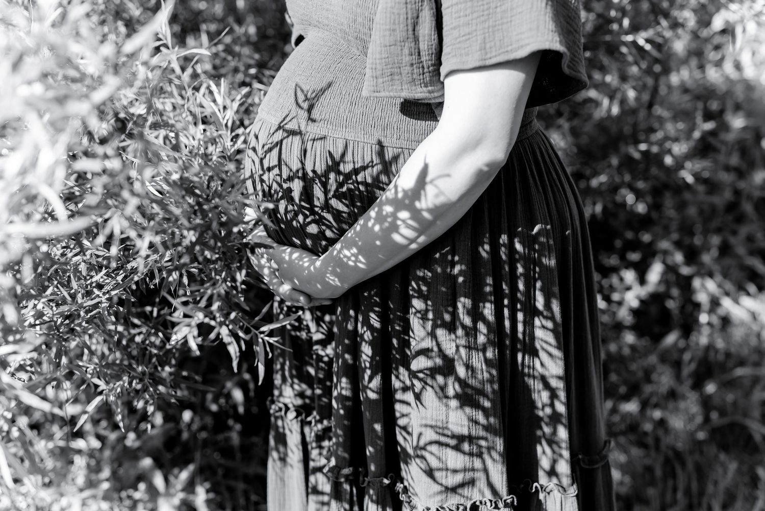 Black and white image showing hands gently touching lavender plants in a garden while wearing a long skirt.
