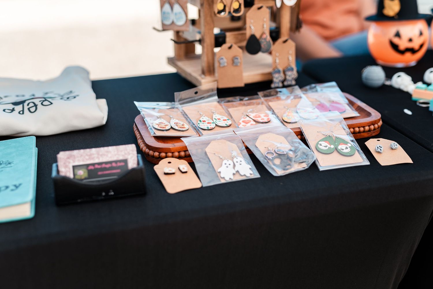 Handmade wooden earrings displayed on black table at craft fair booth with Halloween decor.