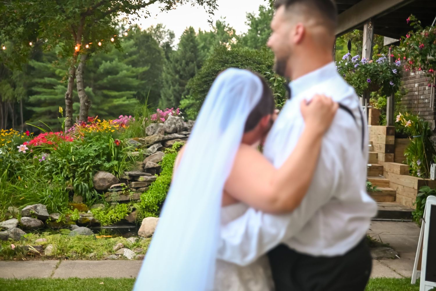 A couple shares their first dance on their wedding day in a beautiful garden setting with vibrant flowers and stone steps.