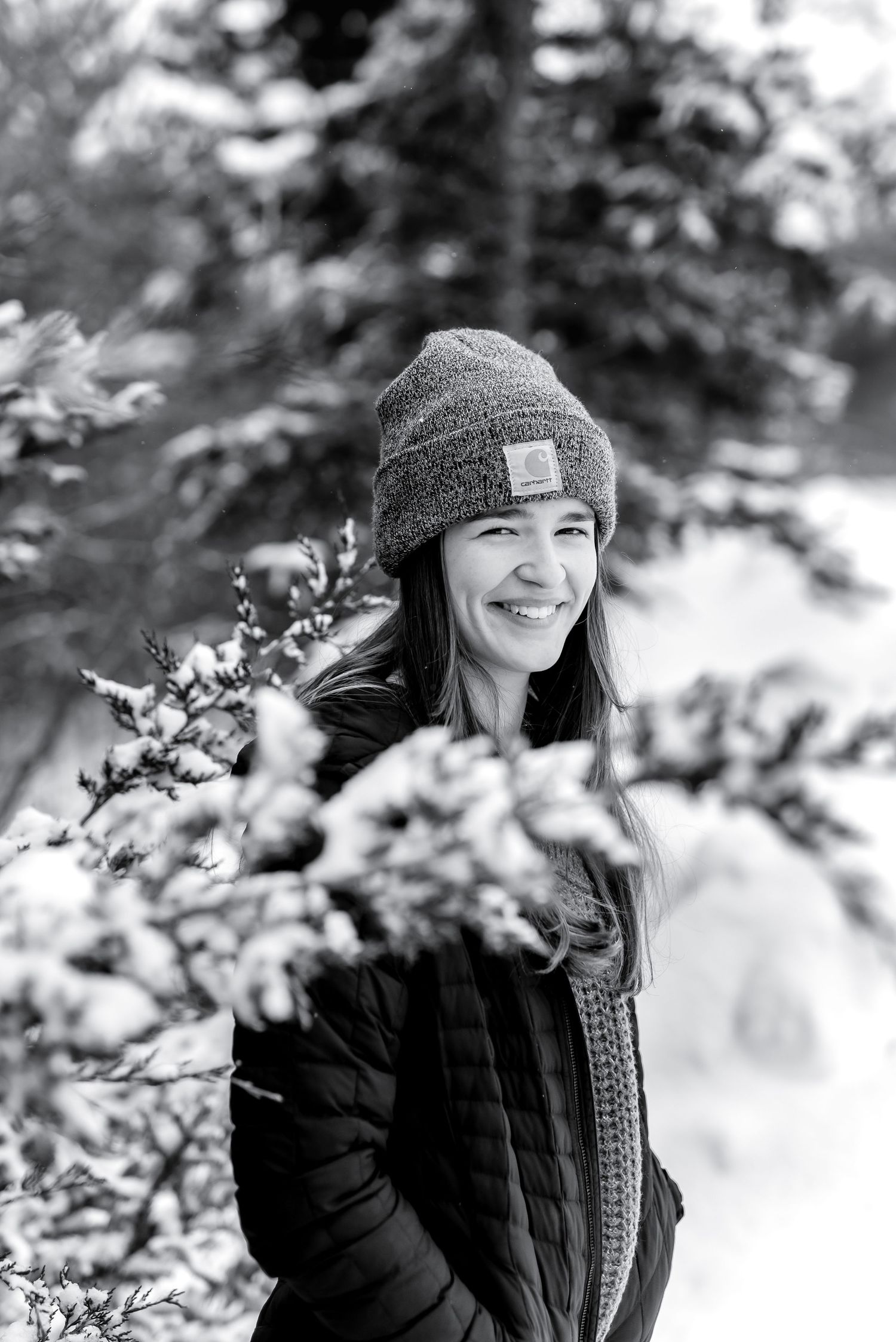 Black and white winter portrait series showing someone in a cozy hat and coat smiling among snowy branches.