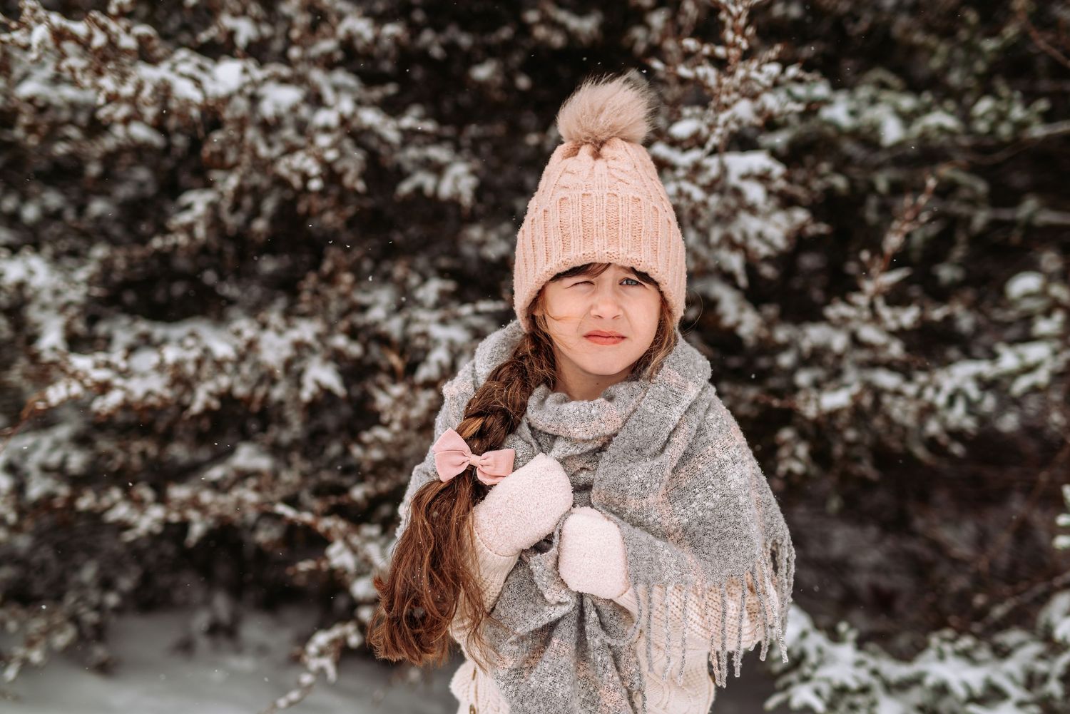 Person in winter attire with pink beanie and scarf poses in snowy outdoor setting during cold weather.