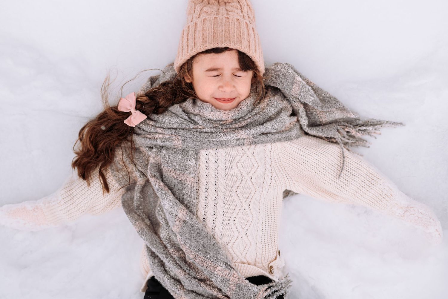 A person in cozy winter sweaters makes snow angels in fresh white snow while smiling joyfully.