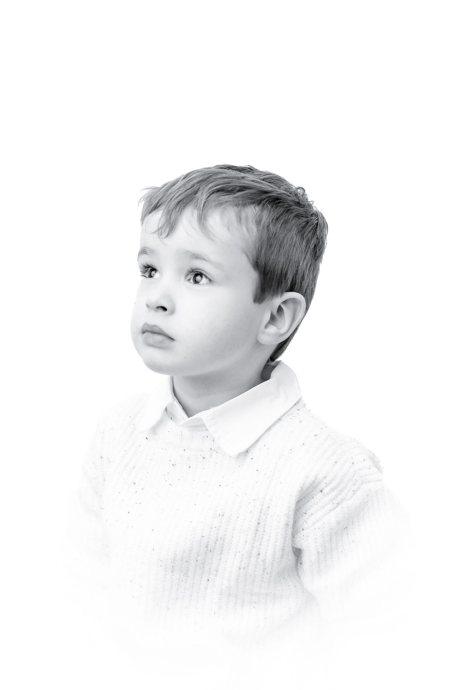 Black and white portrait of a young boy in a white sweater looking upward thoughtfully.