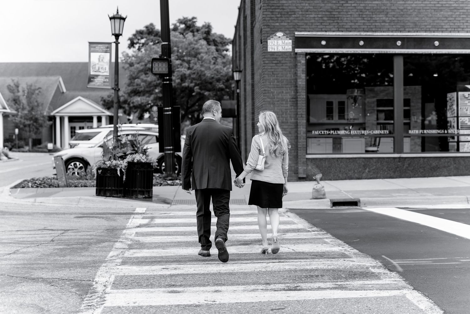 Man and woman holding hands walking through a crosswalk in a small town, black and white photo.