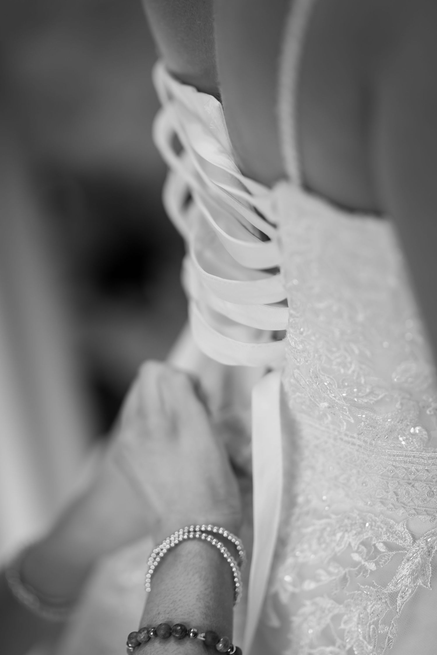 Close-up black and white photo showing white satin ribbons being laced up on what appears to be a wedding dress.