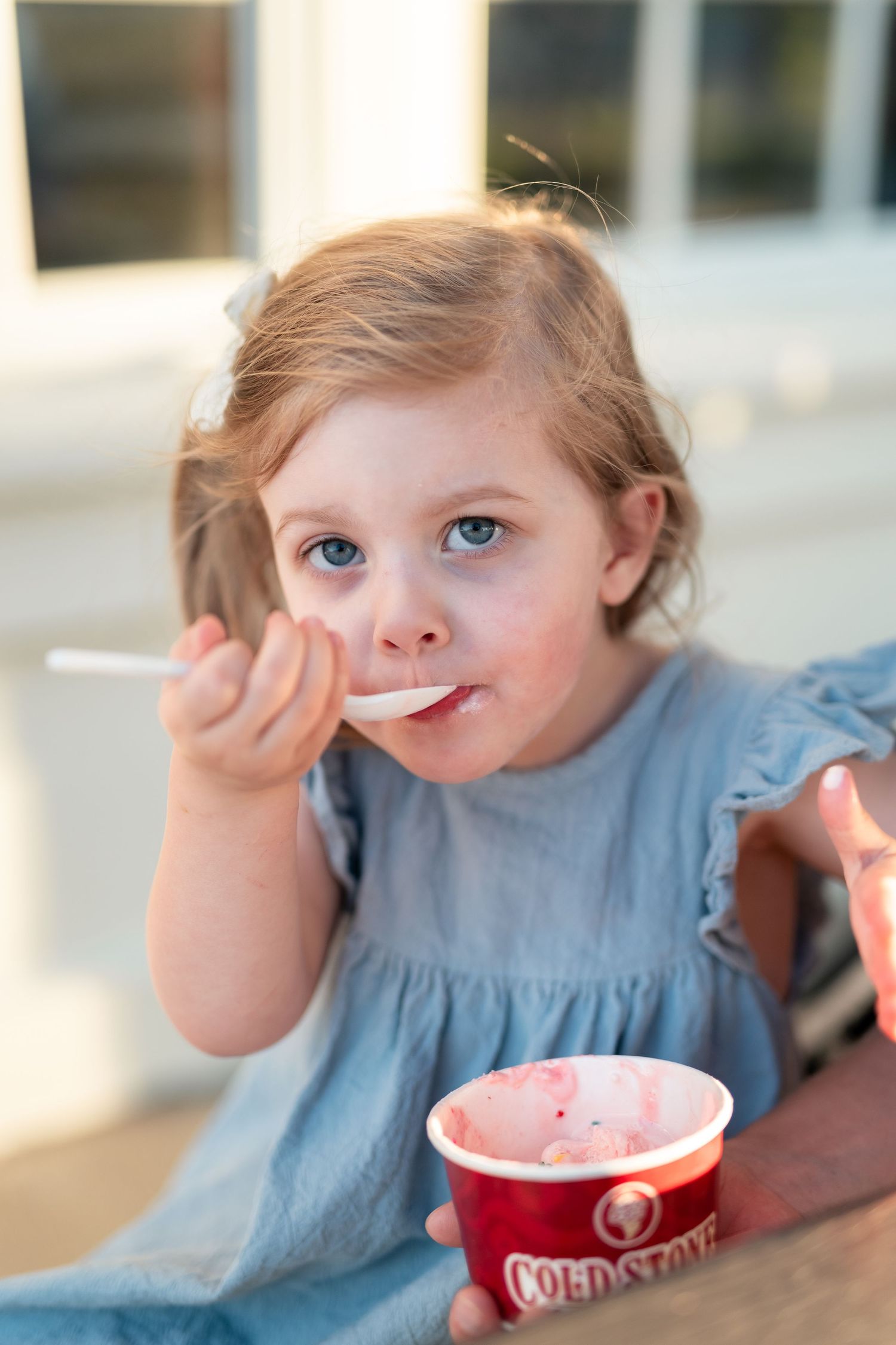Young girl with blue eyes eating strawberry ice cream from a Cold Stone Creamery cup with a spoon.