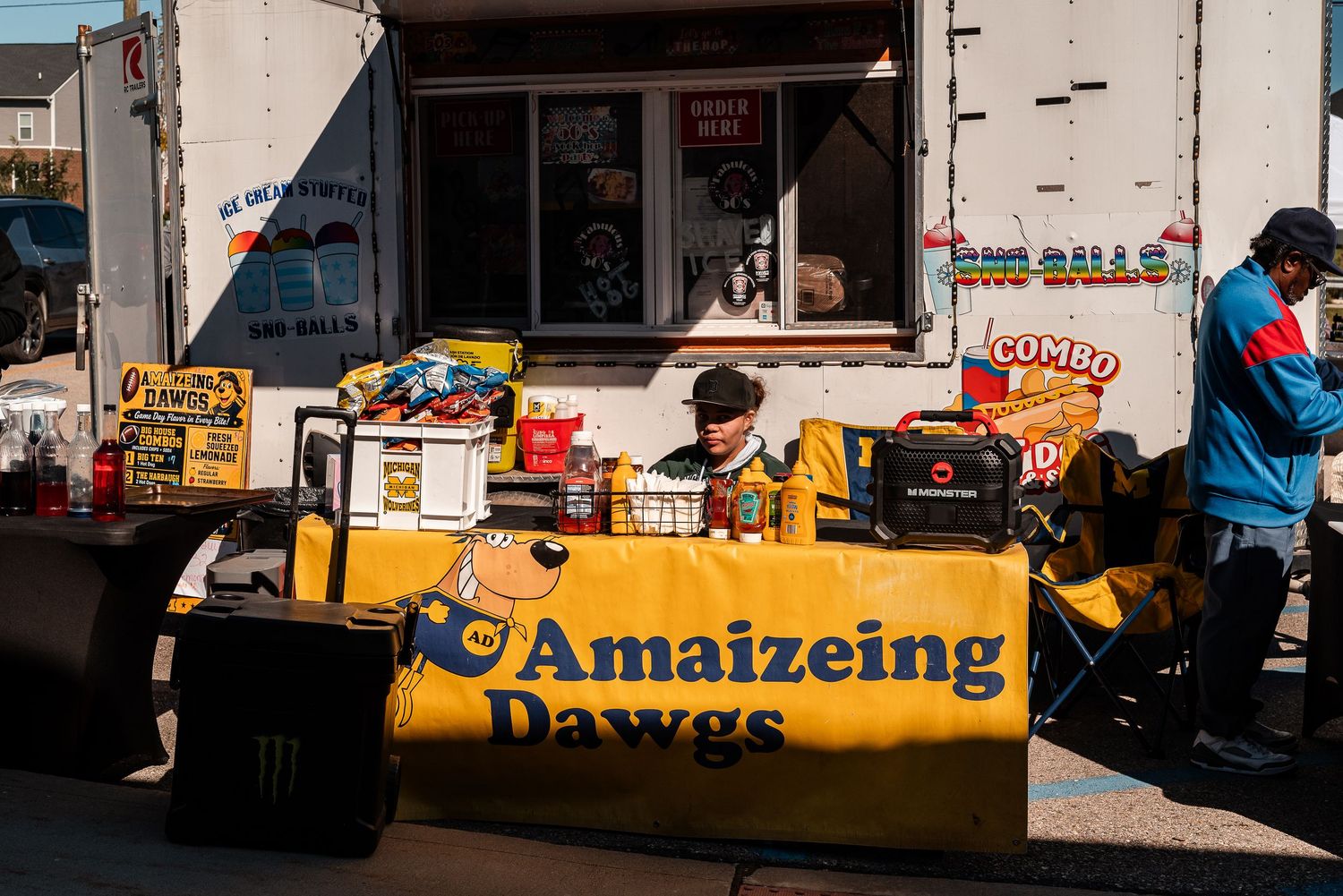Amaizeing Dawgs food truck stand with yellow banner, snacks, and vendor at an outdoor street market.