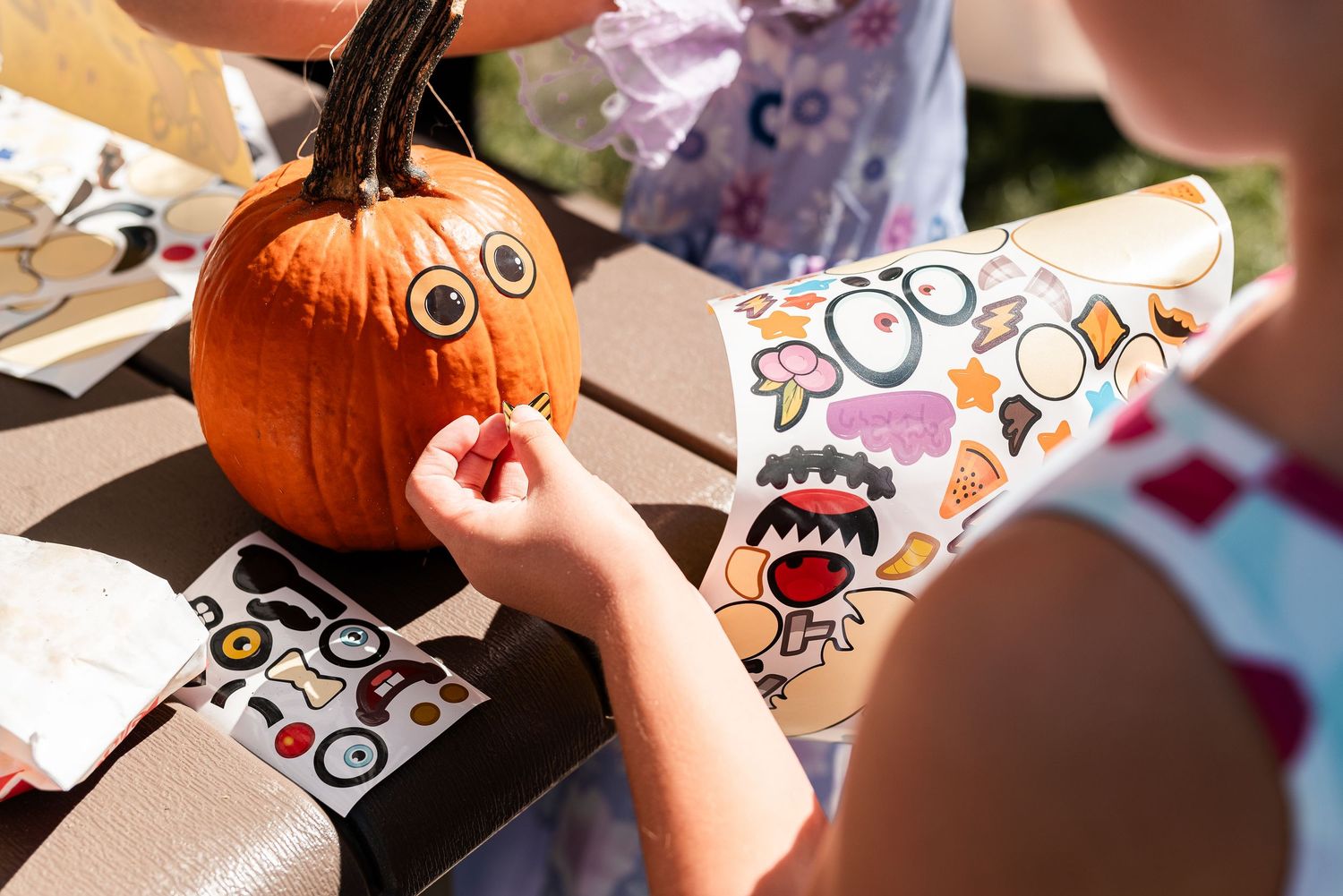 Children decorating a pumpkin with fun face stickers outdoors during a fall Halloween activity.