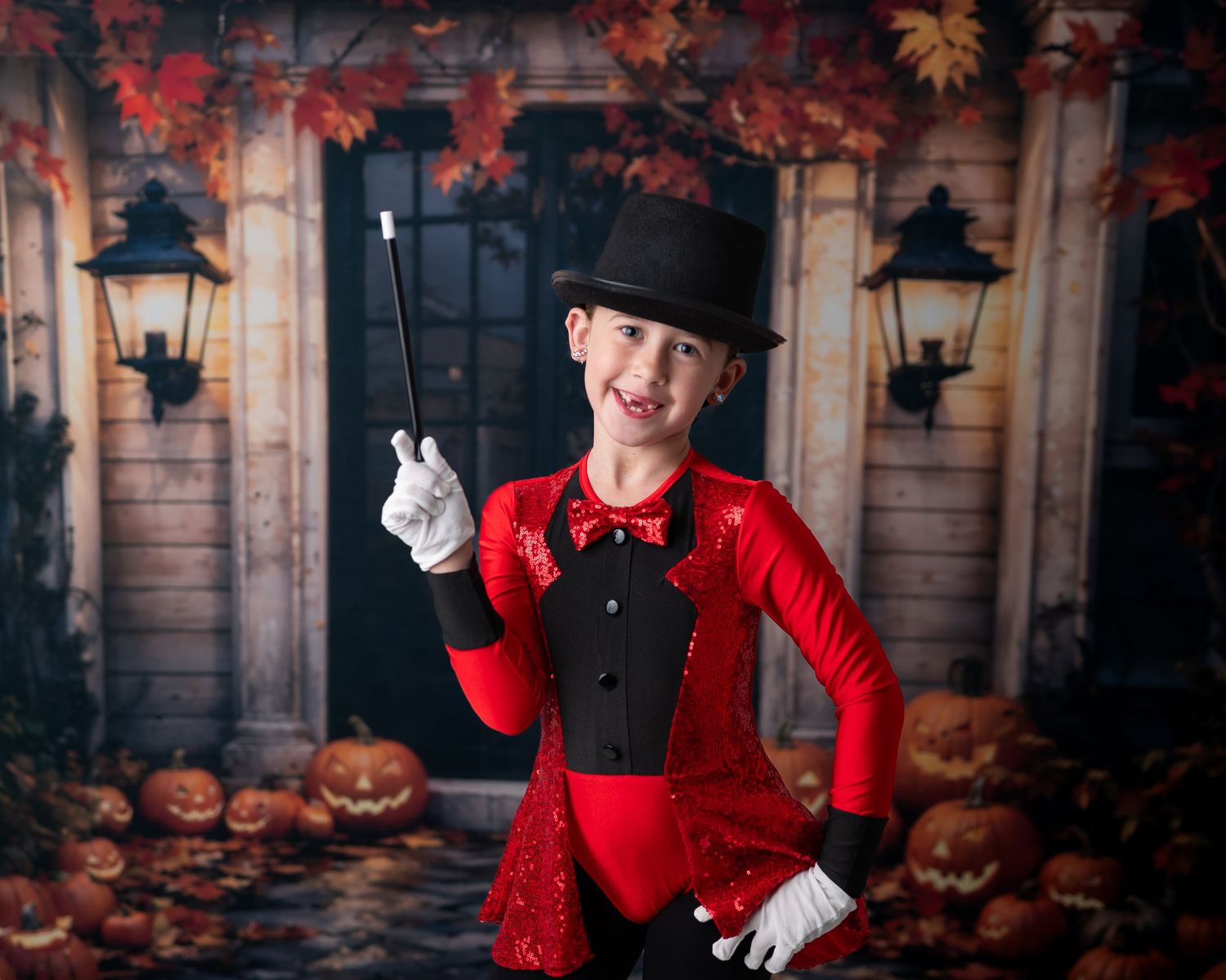 Child dressed as a magician in red sequin jacket and top hat holds a wand, posing with Halloween pumpkins backdrop.