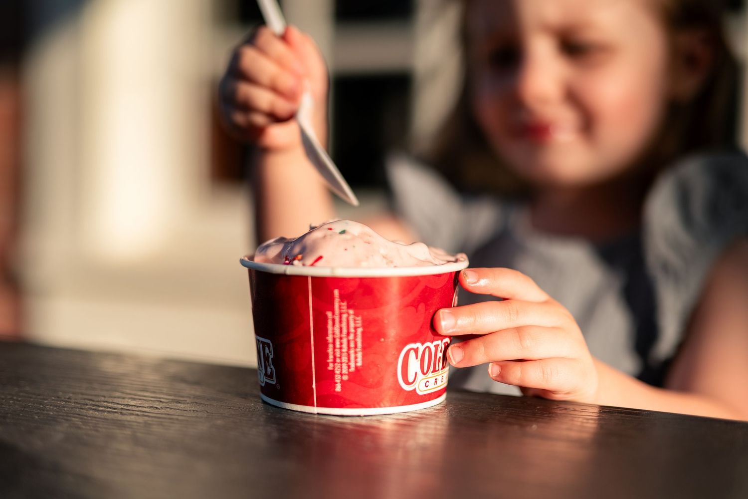 Young girl enjoying a cup of Cold Stone Creamery ice cream with a spoon outdoors.