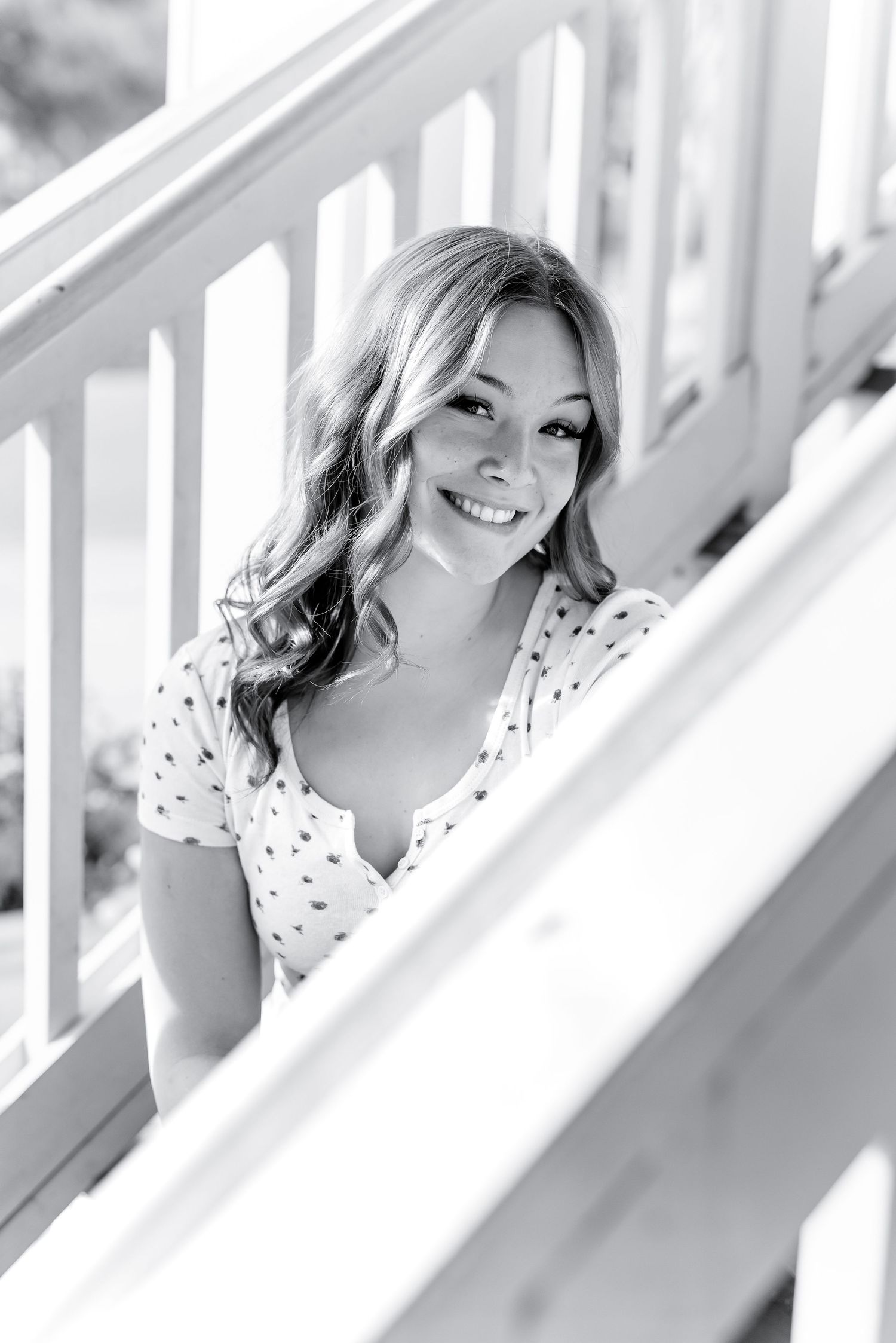 Smiling young woman in polka dot dress on white staircase railing, black and white photo.