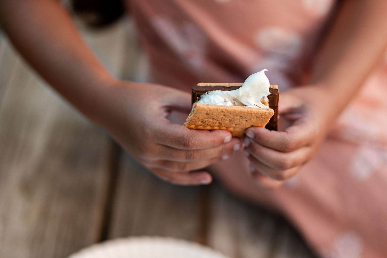 Child holding a gooey s'more with melted marshmallow between graham crackers outdoors.